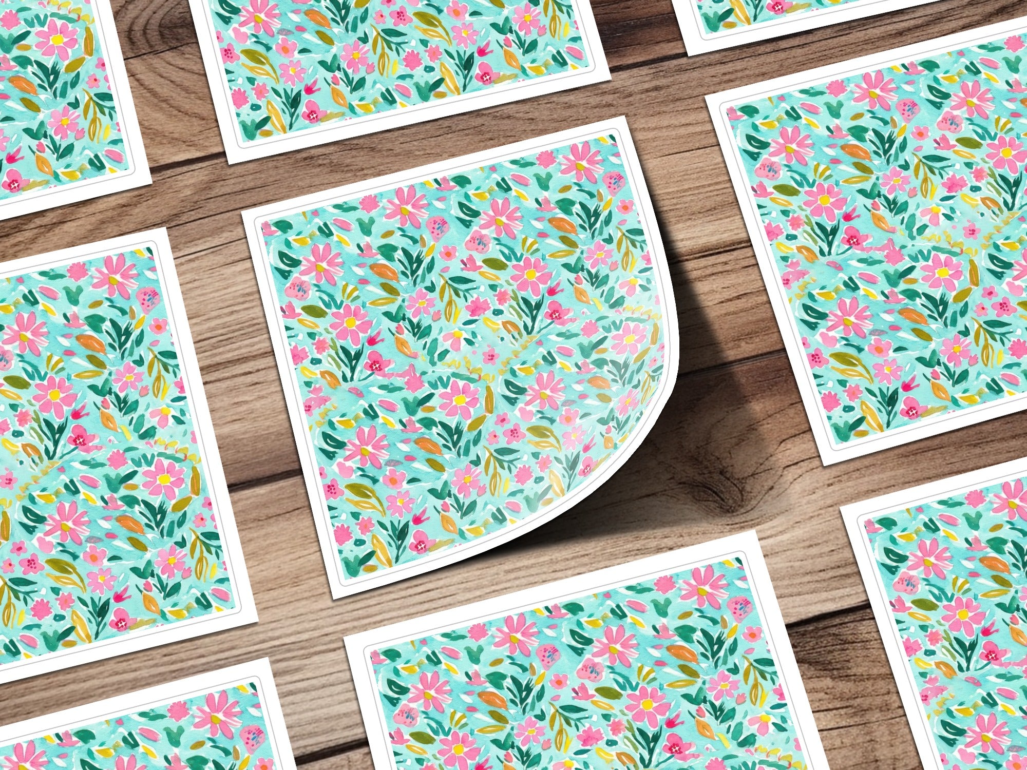 Pattern of small pink and green flowers on white cards, arranged on a wooden surface.
