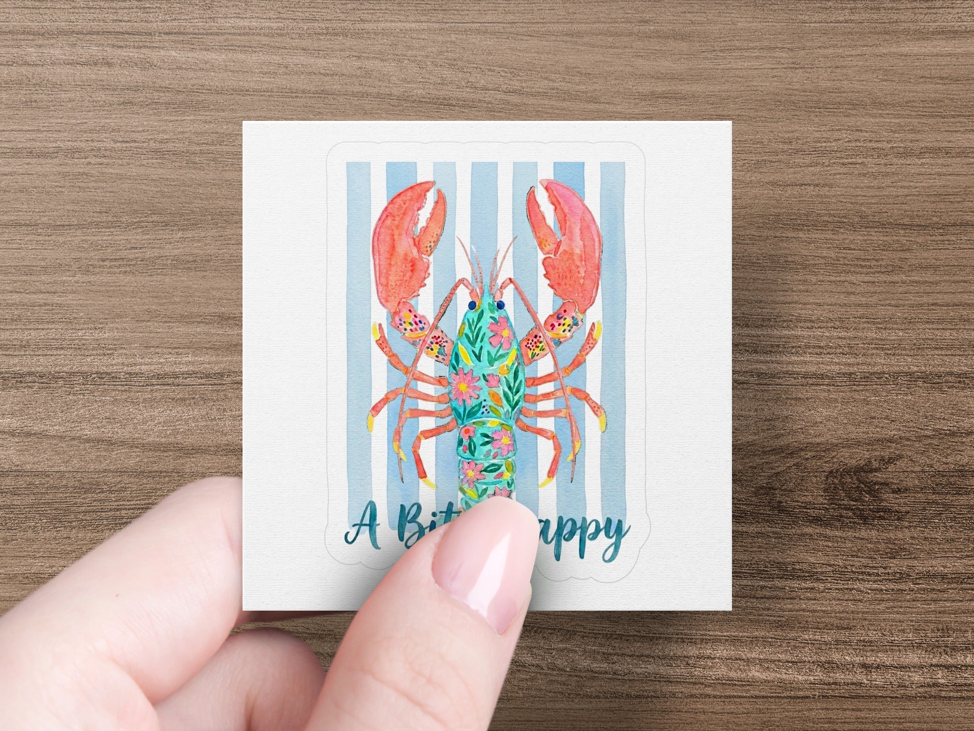 Floral lobster sticker on blue striped background held by fingers.