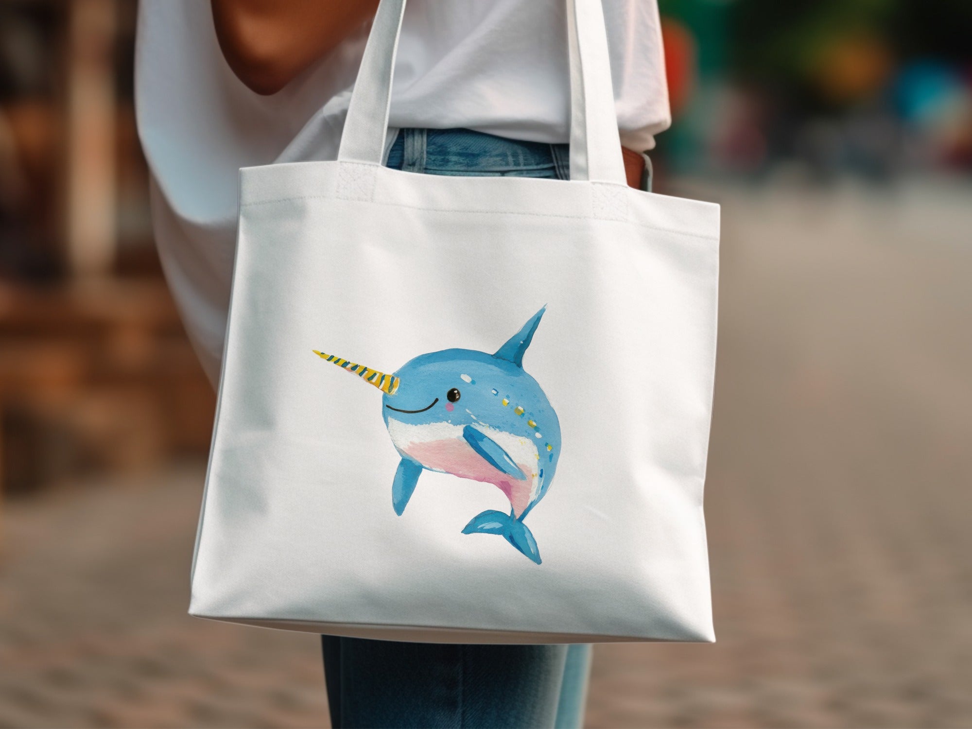White tote bag with a watercolor illustration of a smiling narwhal with a yellow horn.