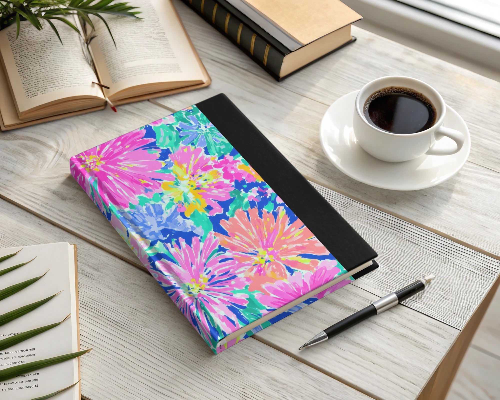 Floral patterned journal with a pen and coffee cup on a wooden desk.