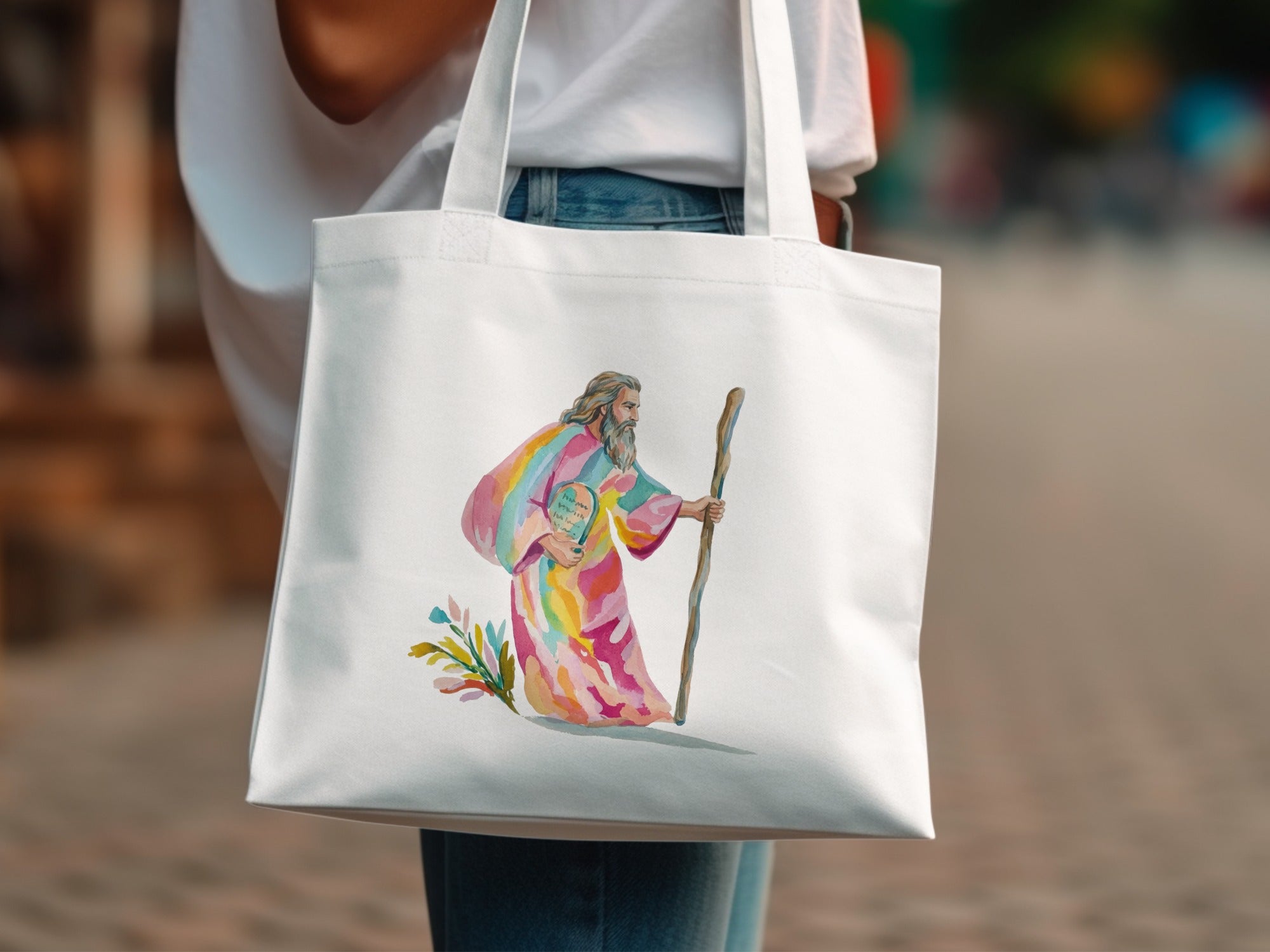 White tote bag with watercolor depiction of a rainbow-robed figure with a staff.