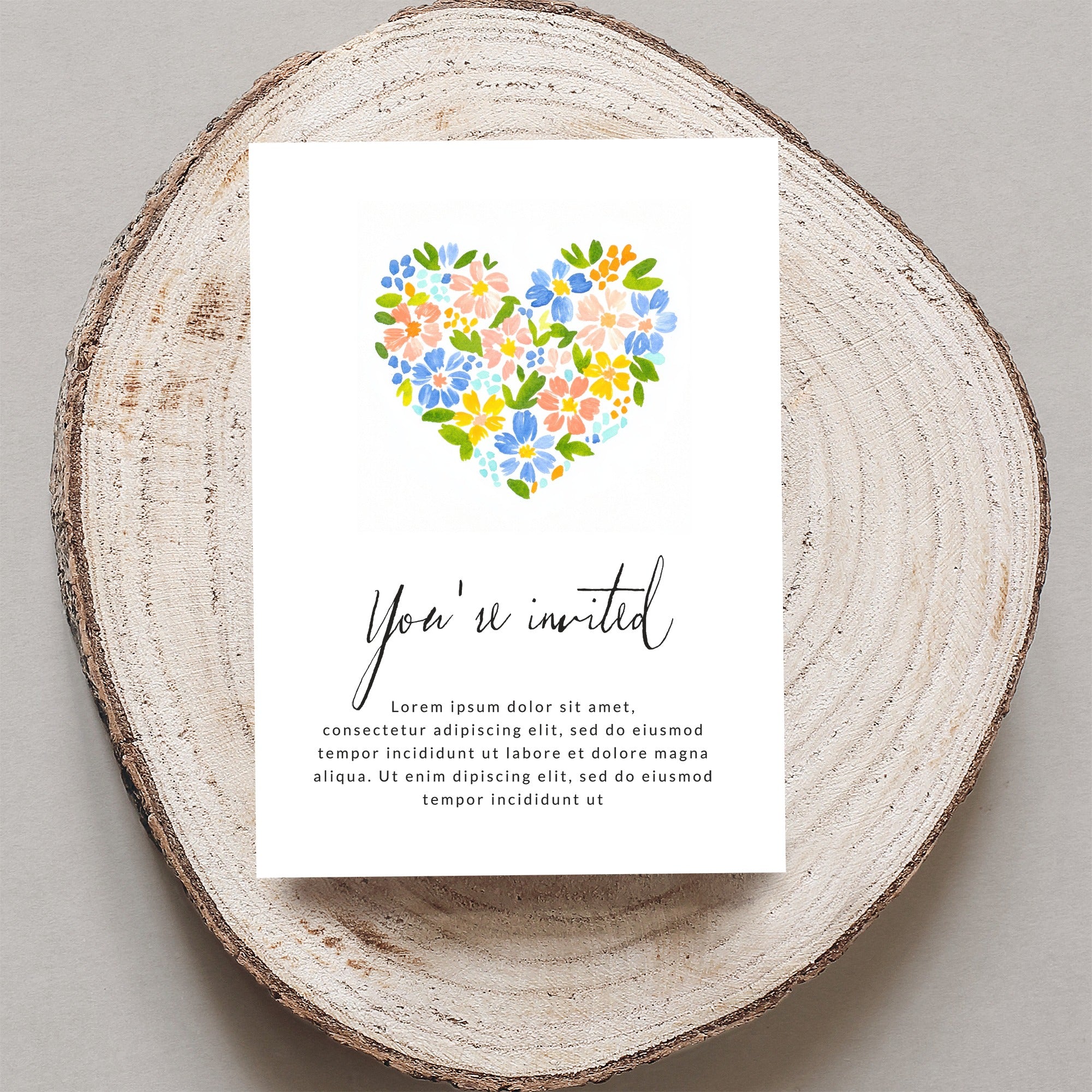 Invitation with floral heart and placeholder text, on a wood slice.