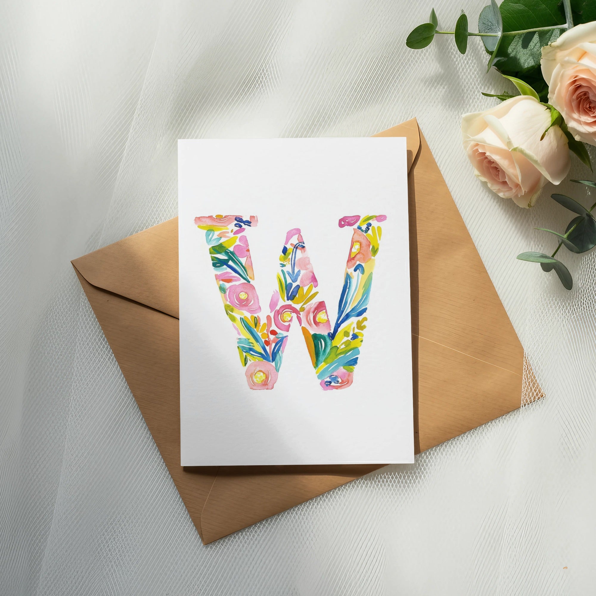Watercolor letter W with floral accents on a white card over a brown envelope.