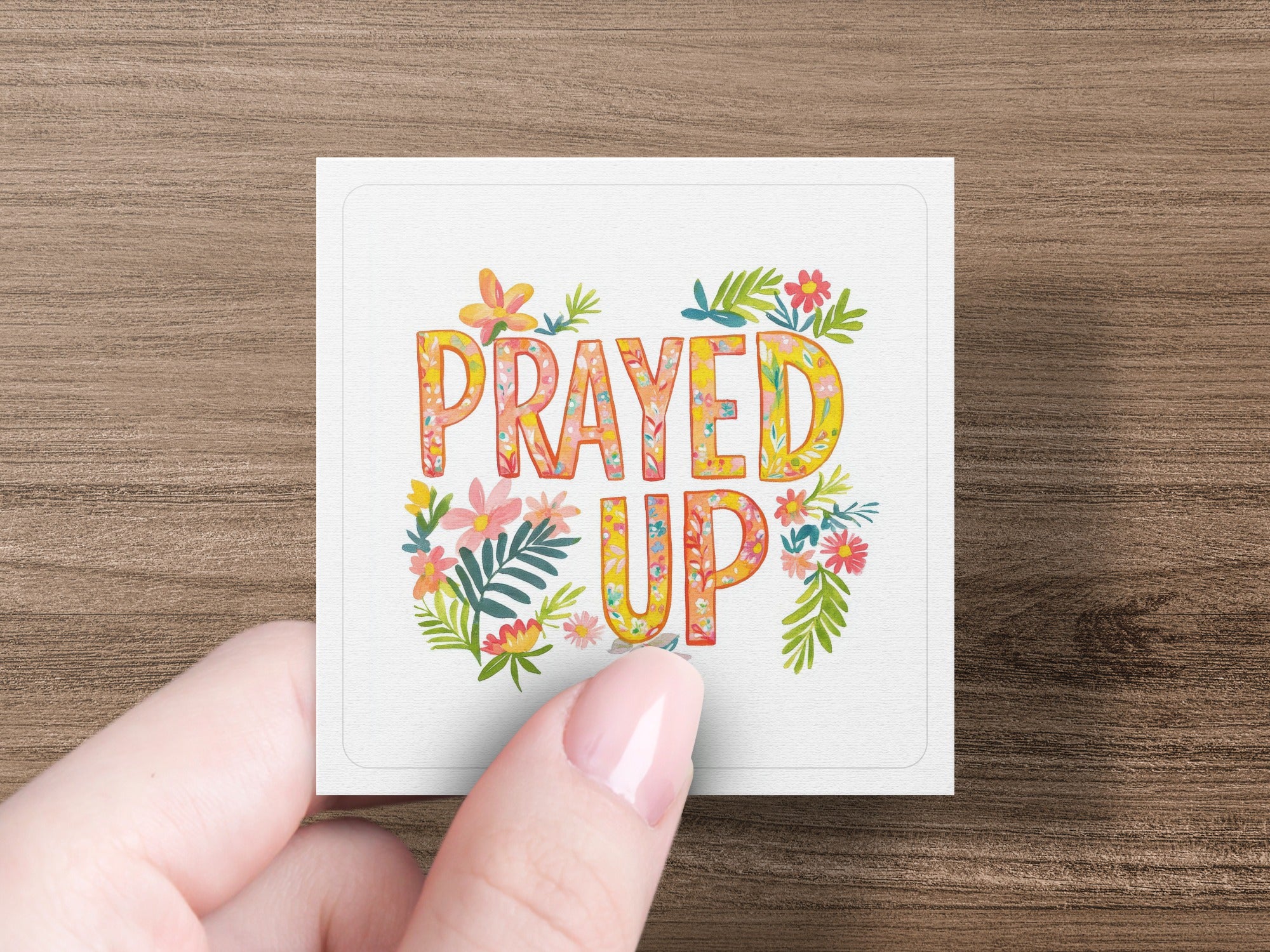 Square card with "PRAYED UP" text and floral accents held by a hand.