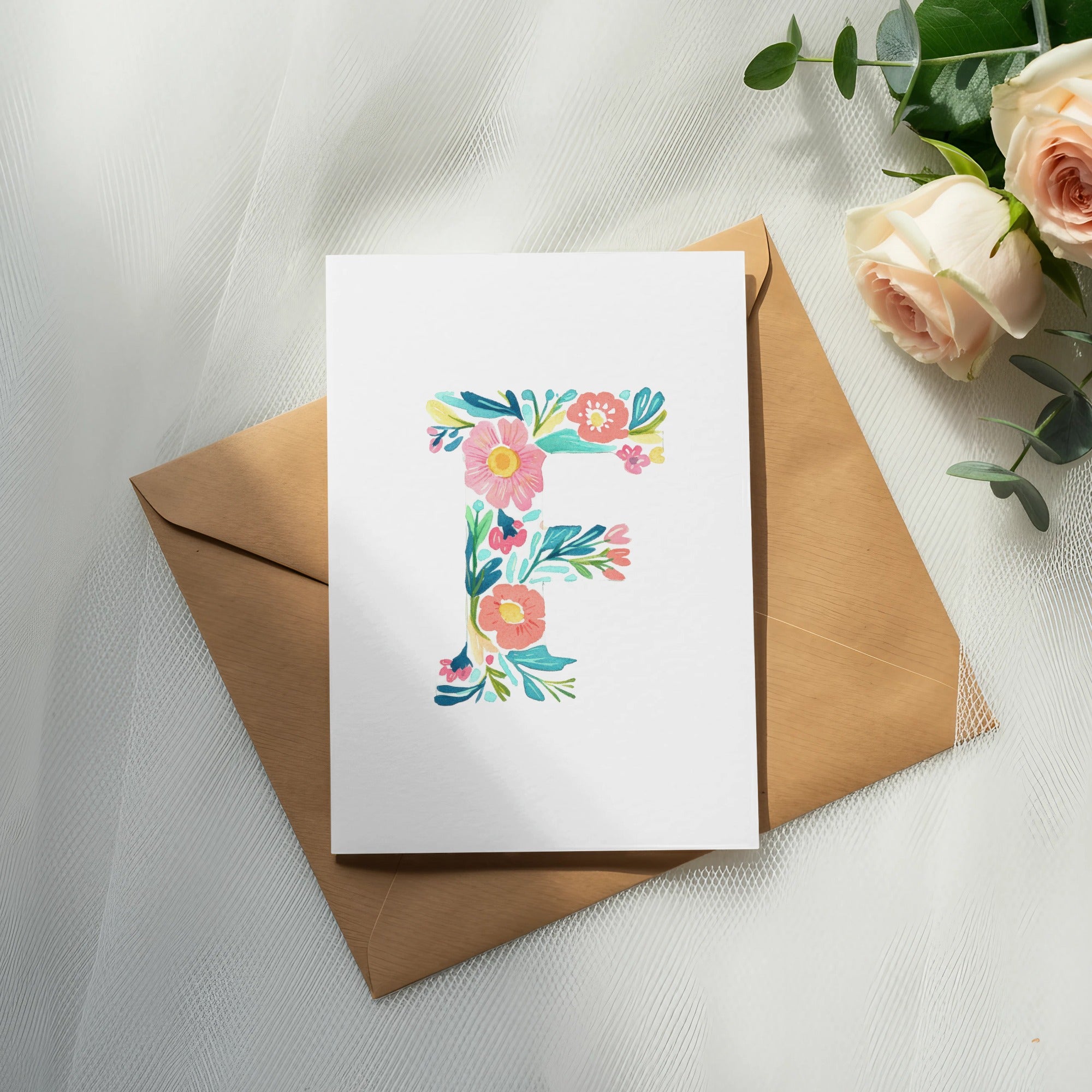 Floral letter F on white card, resting on brown envelope, with roses.