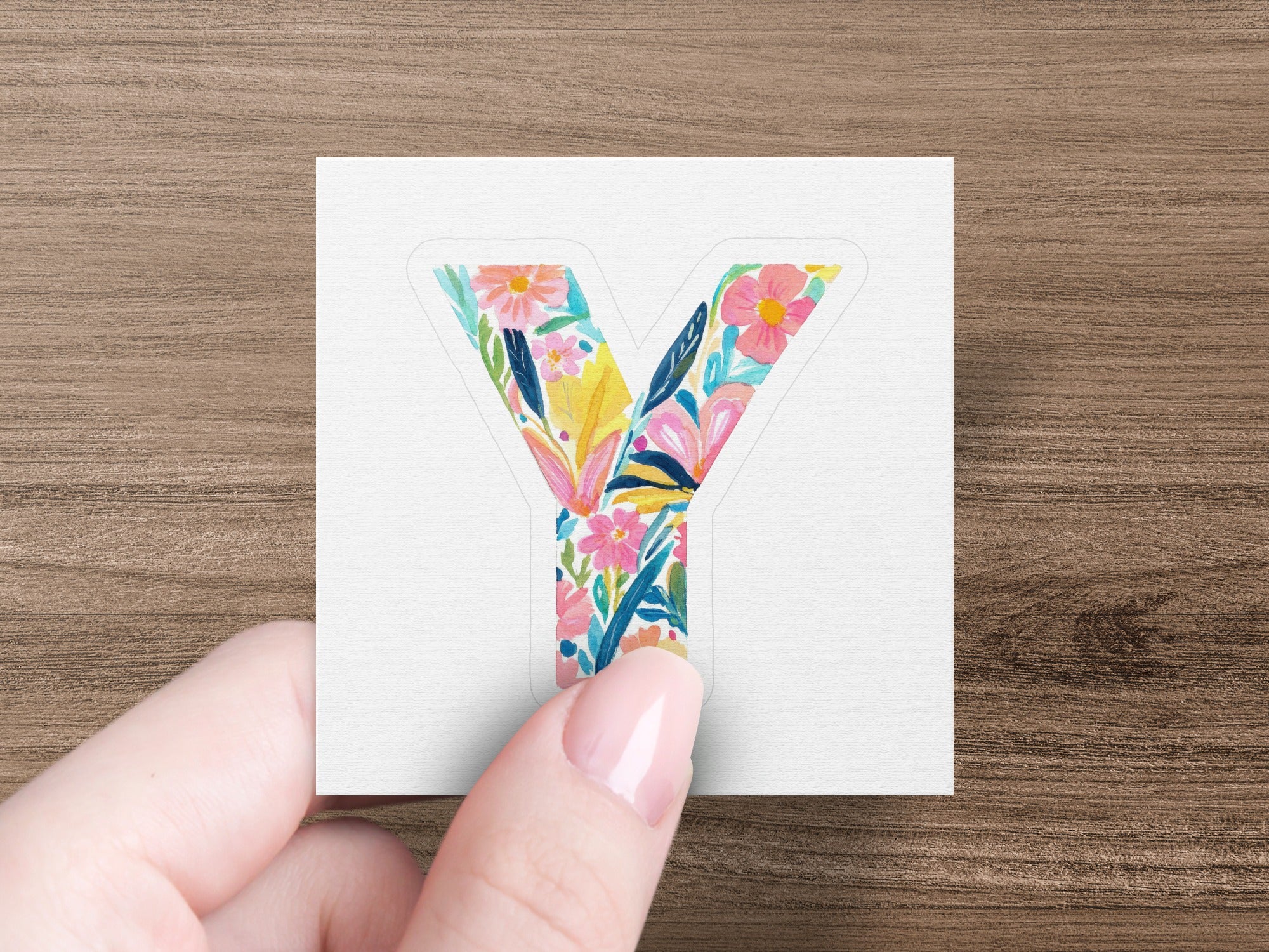 Letter Y sticker with colorful floral design held by fingers.