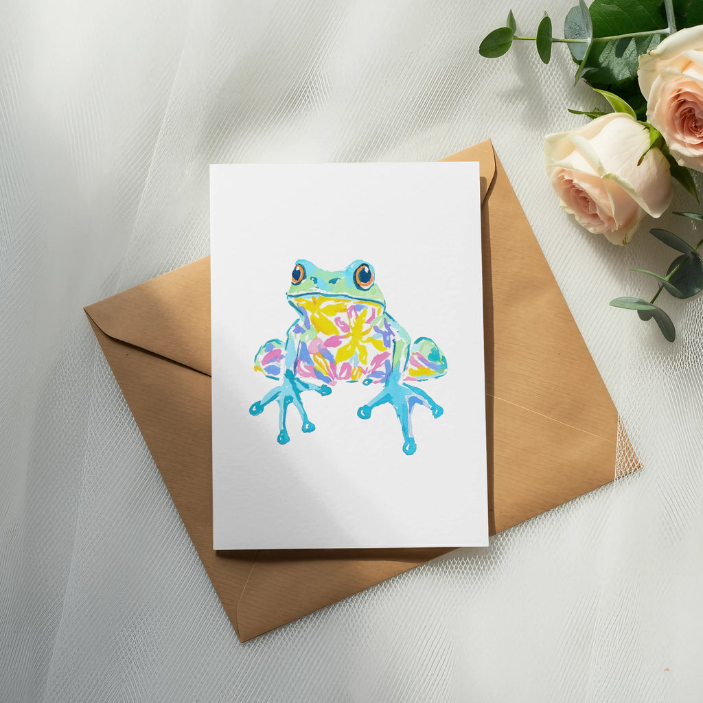 Watercolor painting of a colorful frog on a card with a brown envelope.