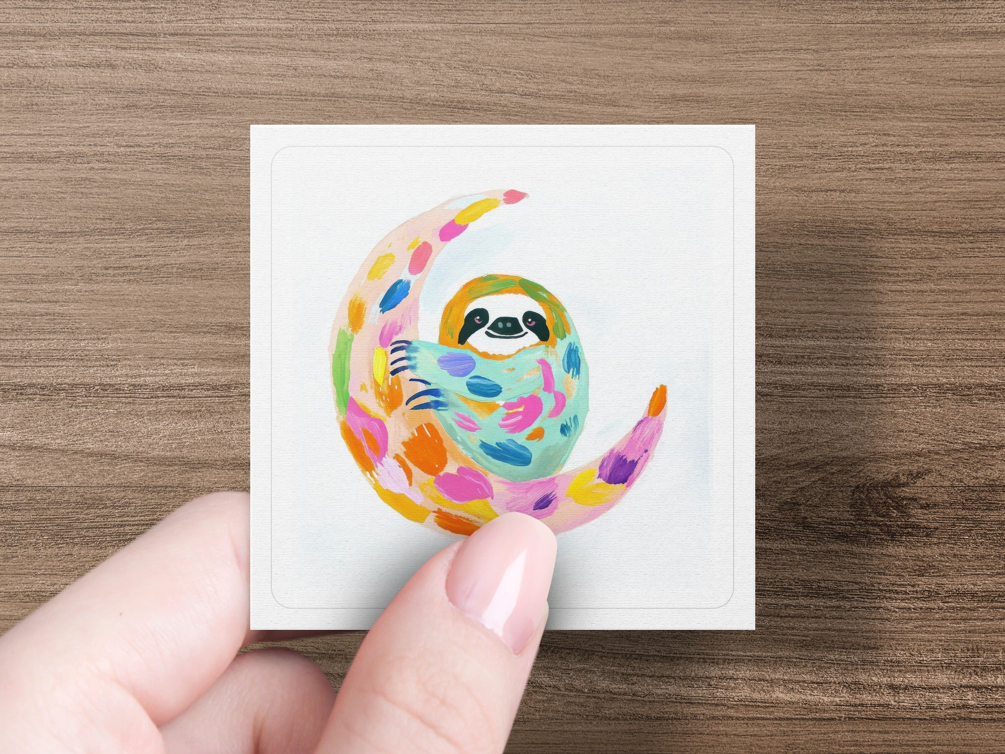 Small square painting of a colorful sloth on a crescent moon.