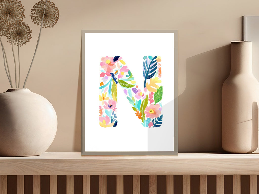 Watercolor floral letter N in a frame on a shelf.