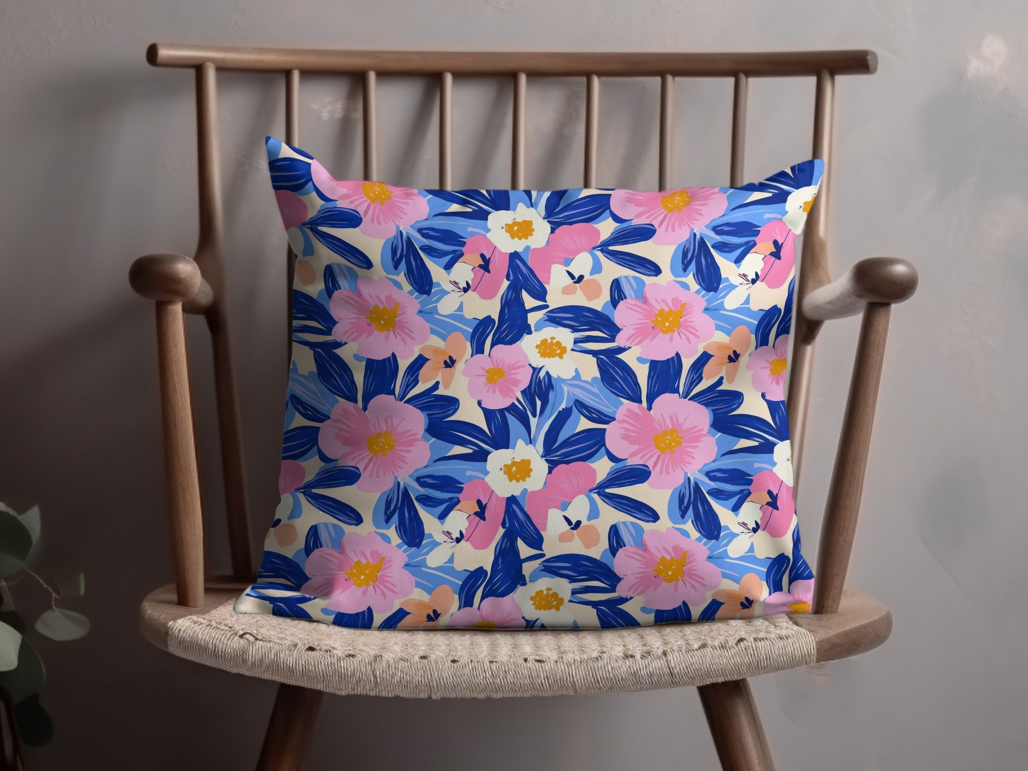 Floral pattern pillow with pink, blue, and cream flowers on a wooden chair.