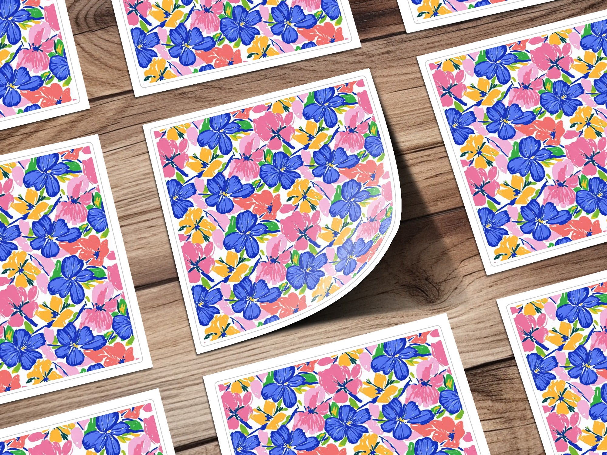 Floral pattern on cards with blue, pink, and yellow flowers on a wooden surface.