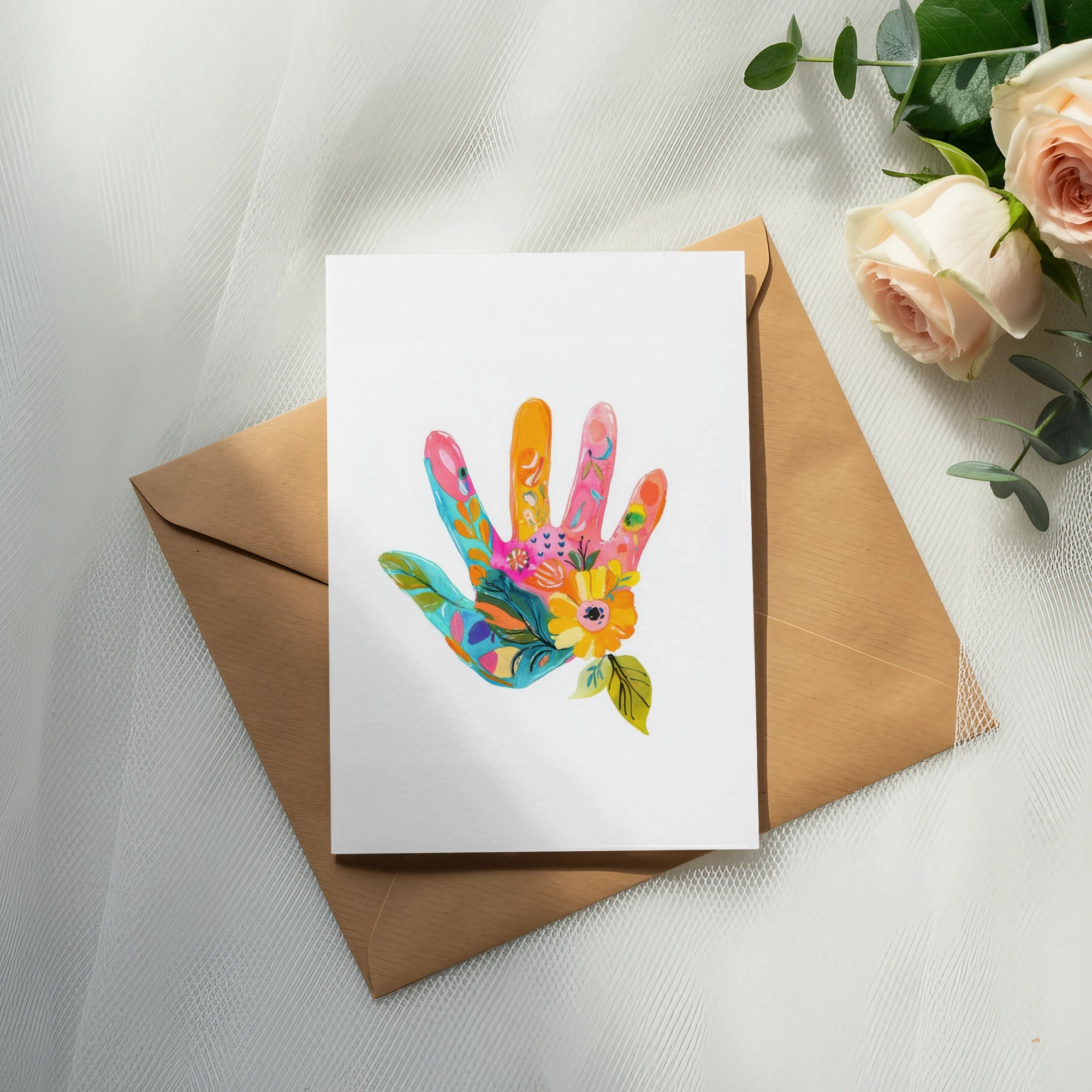 Card with a colorful floral hand print on an envelope, next to roses.