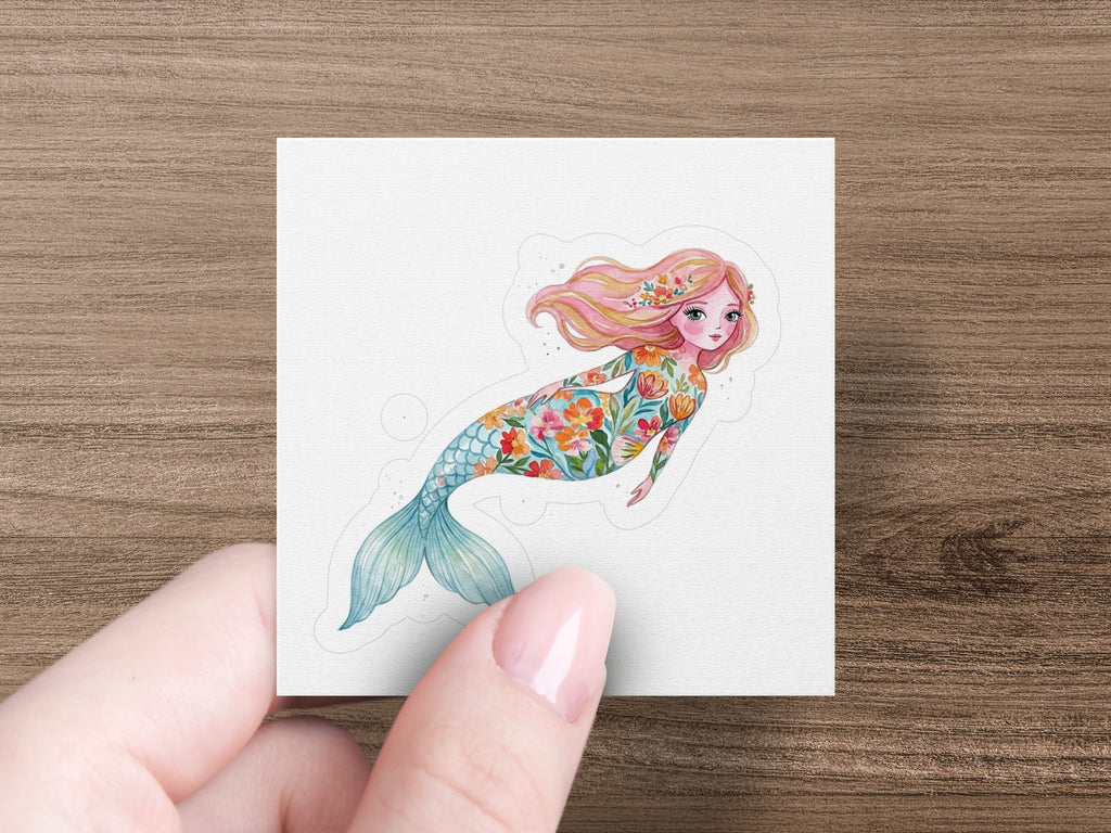 Floral mermaid with pink hair and a colorful tail, held by a finger.