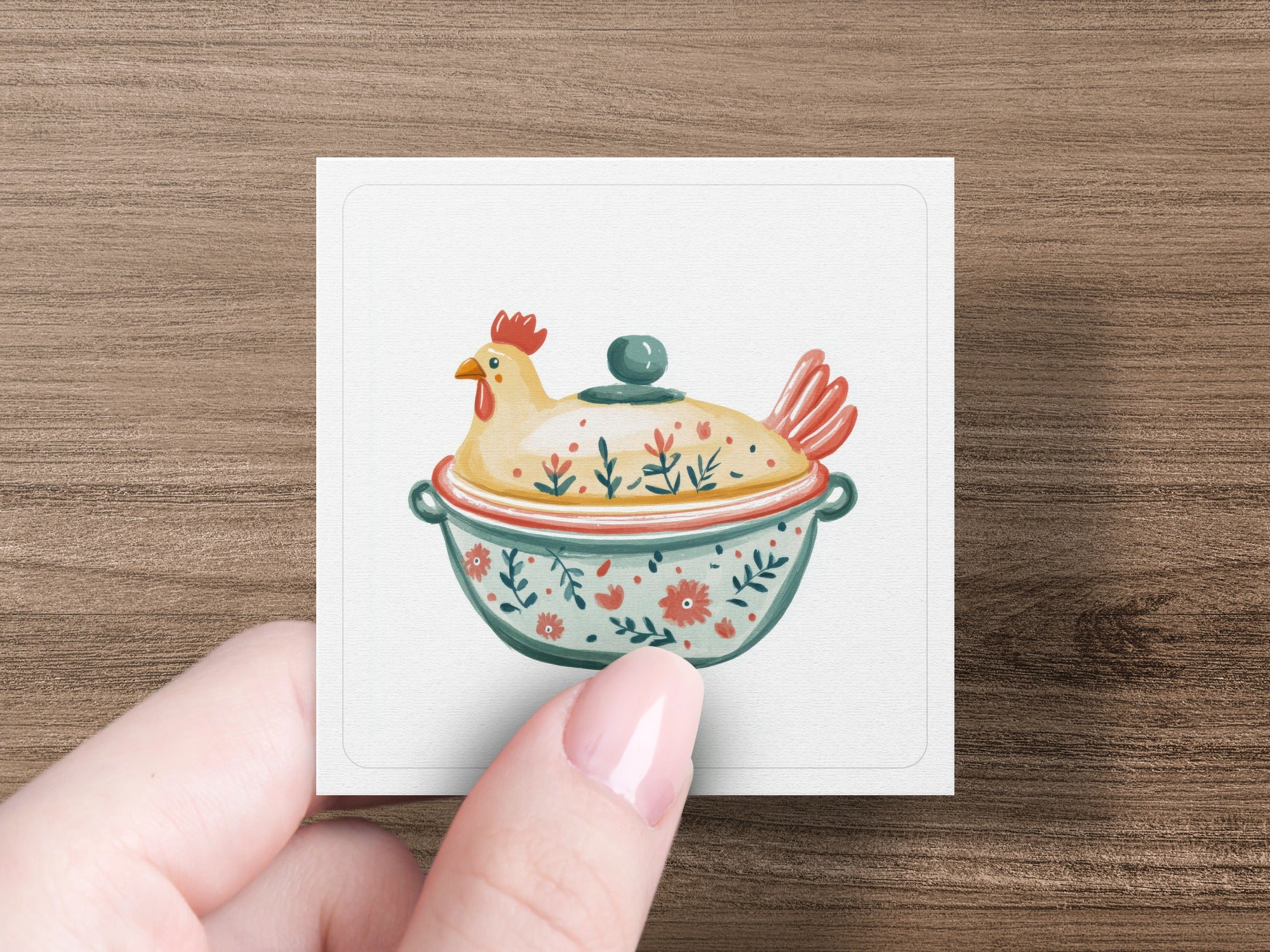 Hand holding square card with chicken pot illustration on wooden background.