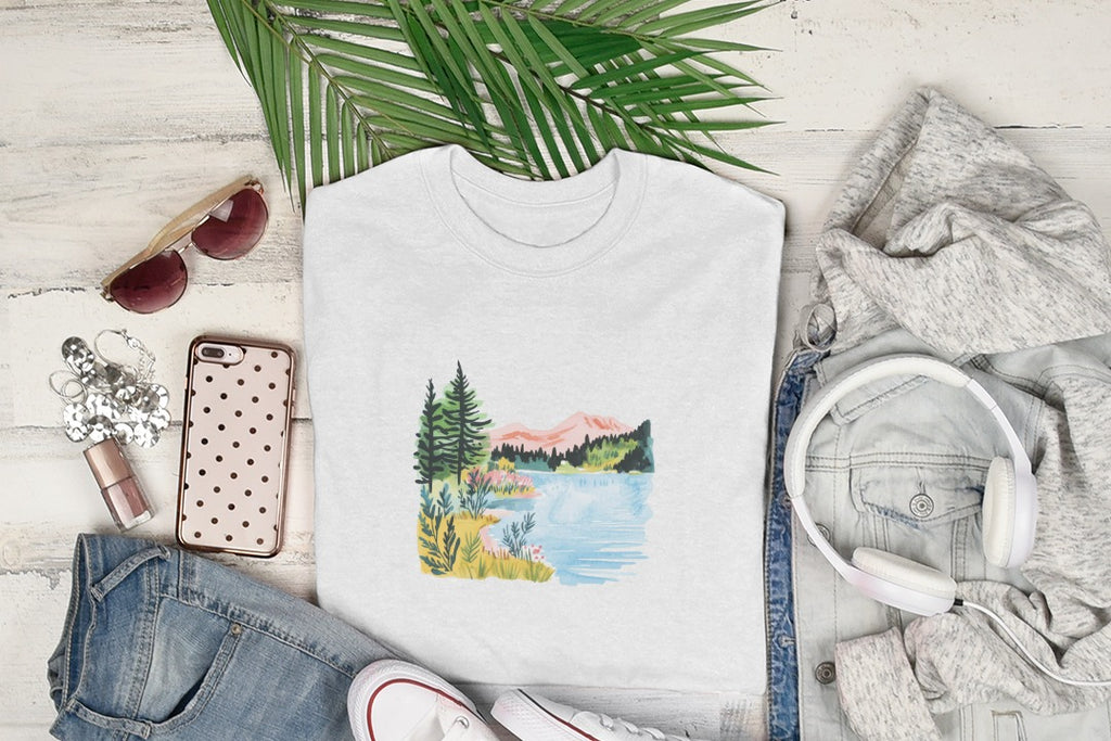 White t-shirt with watercolor landscape of mountains, lake, and trees.