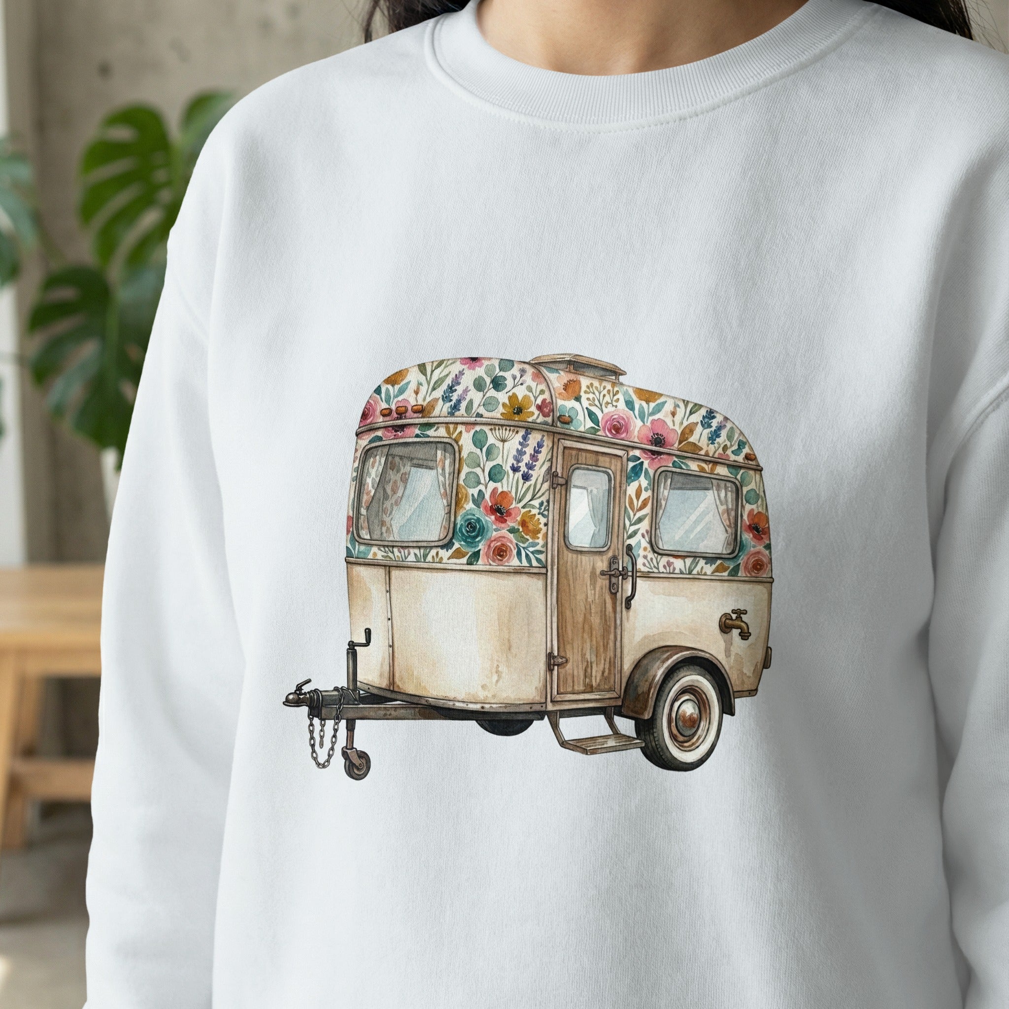 White sweatshirt featuring a watercolor illustration of a vintage camper decorated with floral patterns.