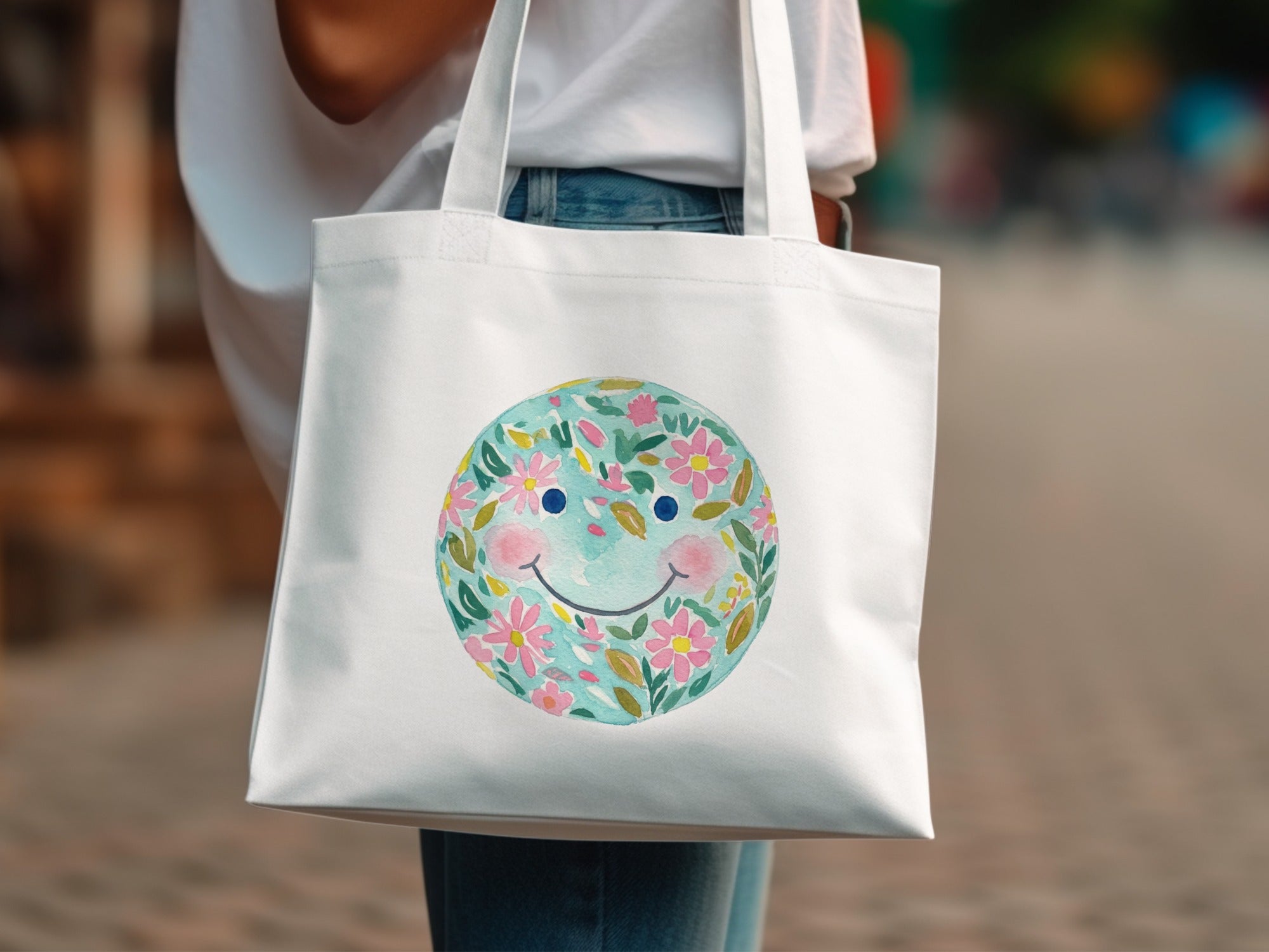 White tote bag with a watercolor smiley face design filled with pink flowers and green leaves.