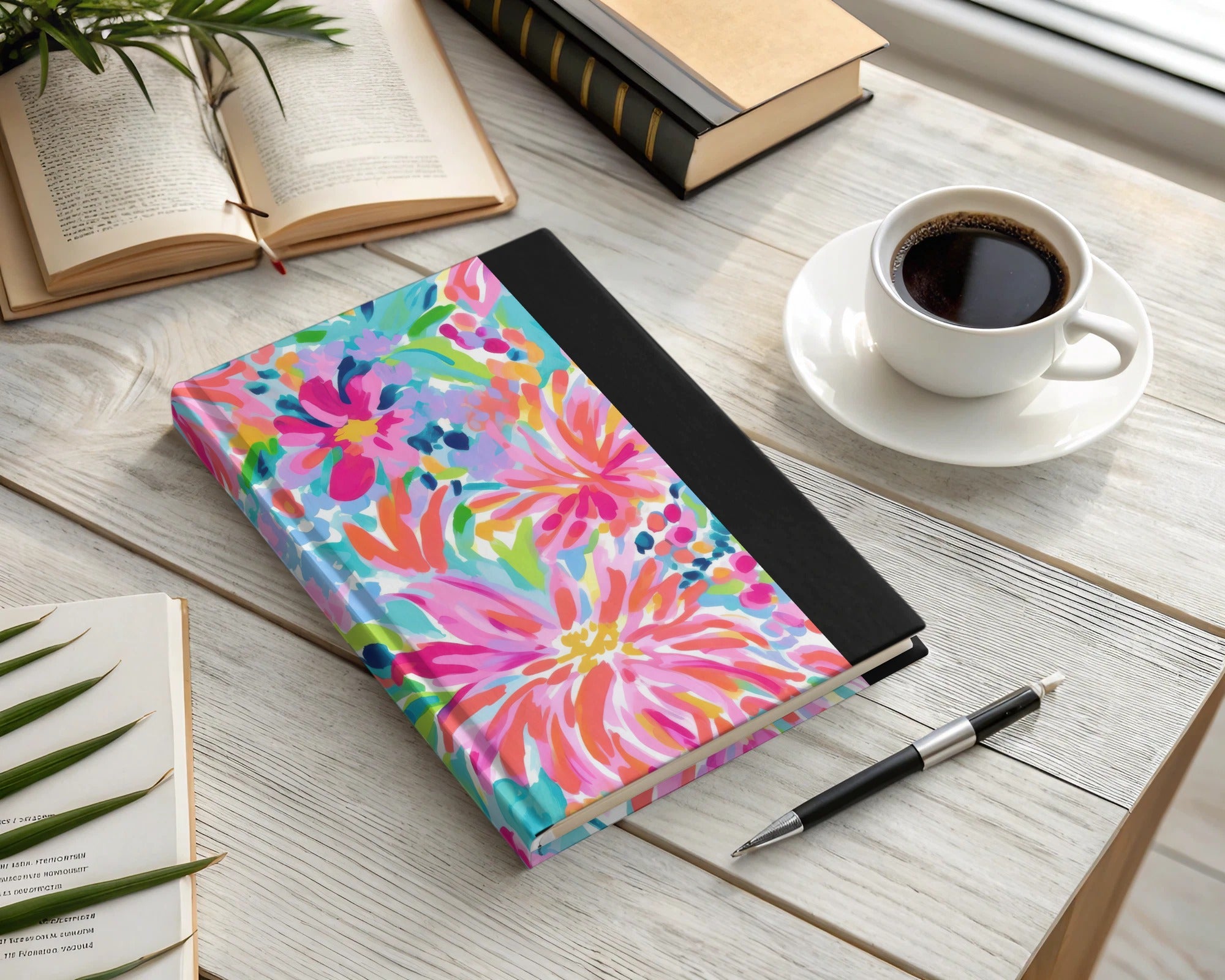 Lilly Pulitzer journal with floral design and black cover next to coffee and pen.