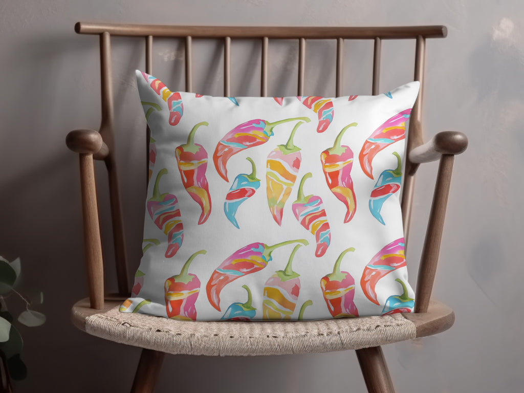 White throw pillow with colorful chili pepper pattern on a wooden chair.