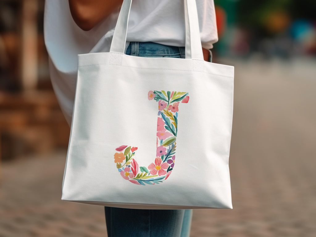 White tote bag with a floral letter 'J' design.