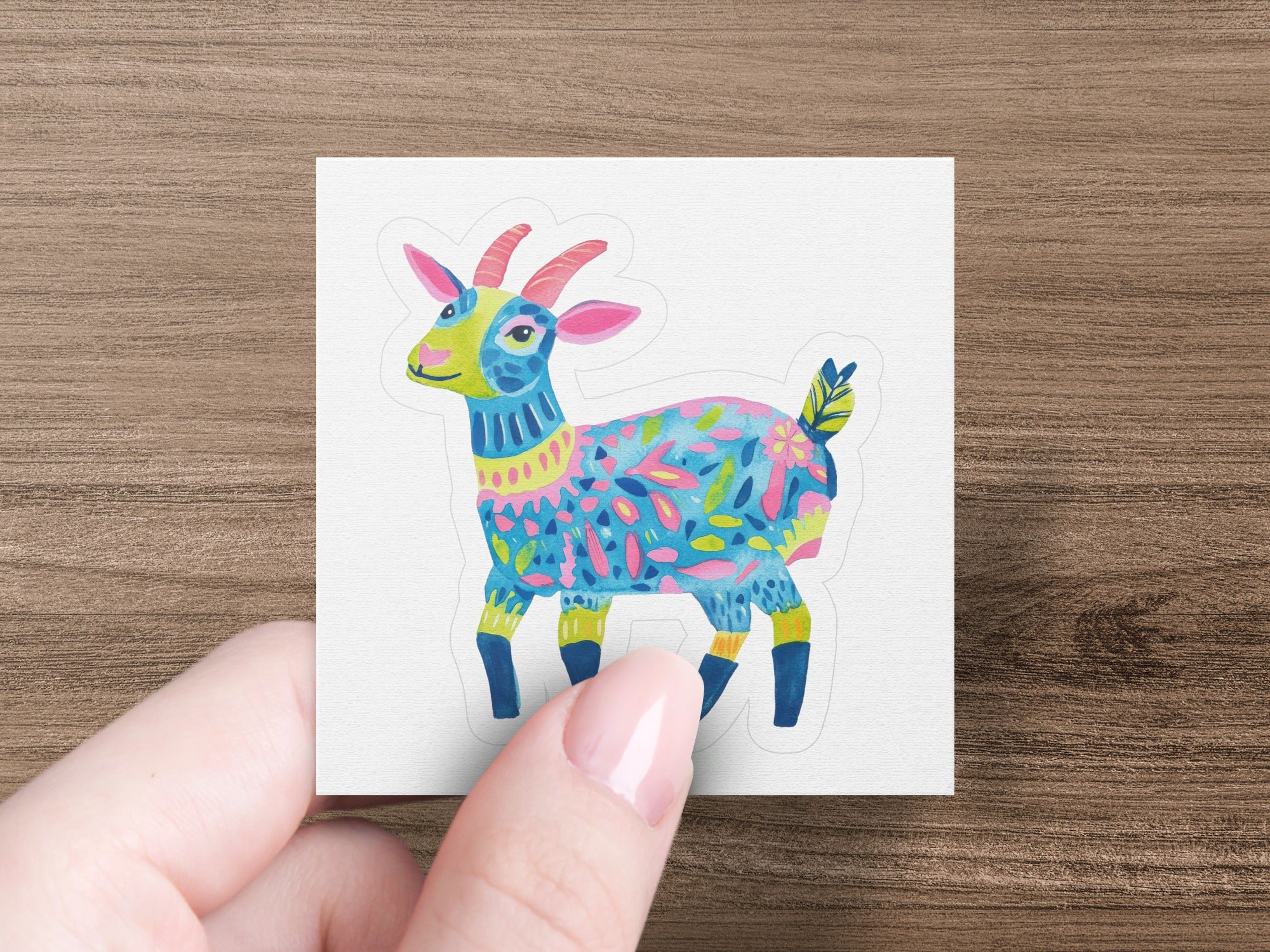 Colorful, patterned goat sticker held by a person's fingers.