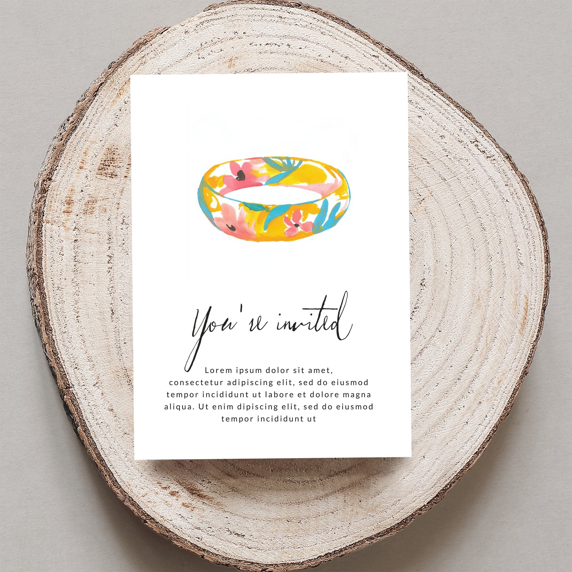 Floral ring invitation on wood slice with "You're invited" text.