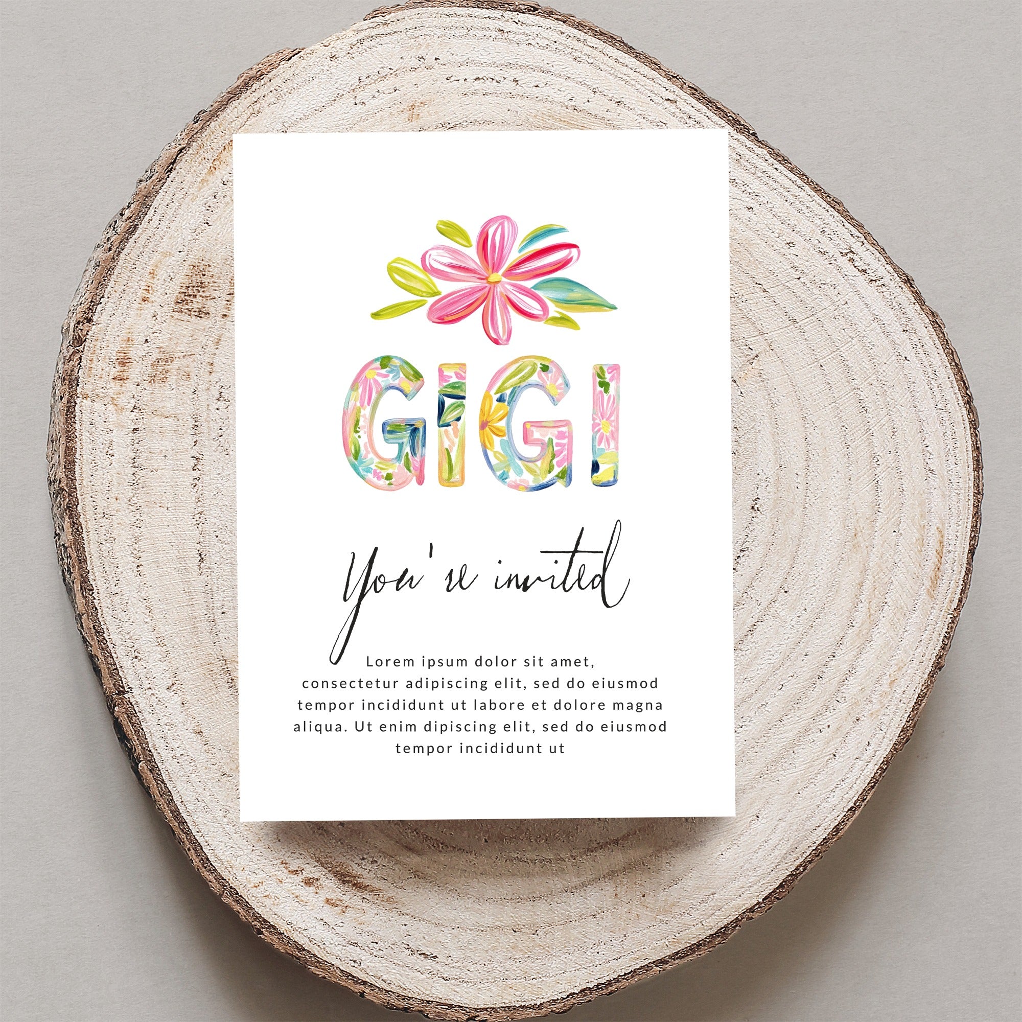 "Gigi You're invited" card with floral letters on wood slice.