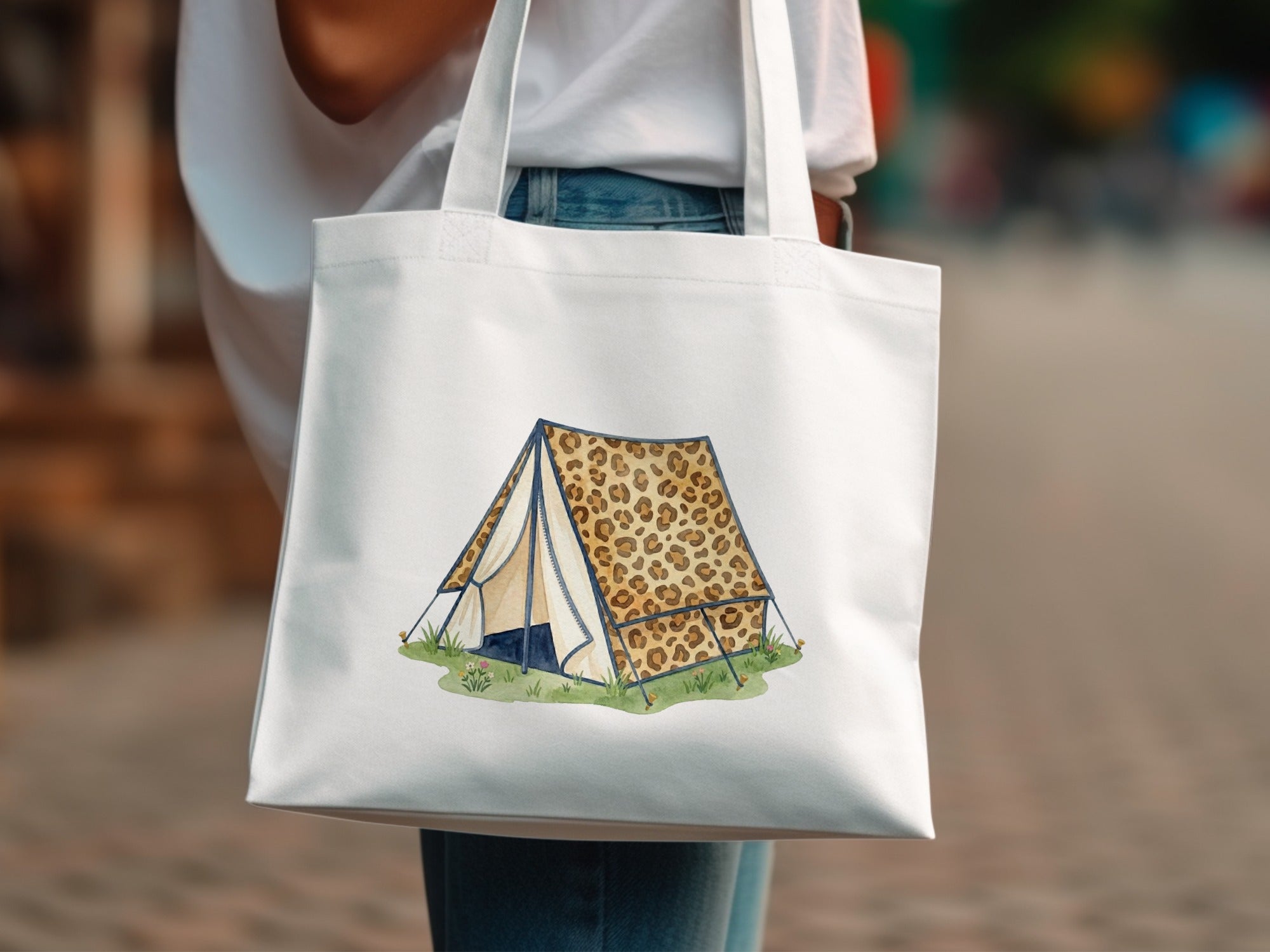 White tote bag with leopard print tent illustration on grassy field.