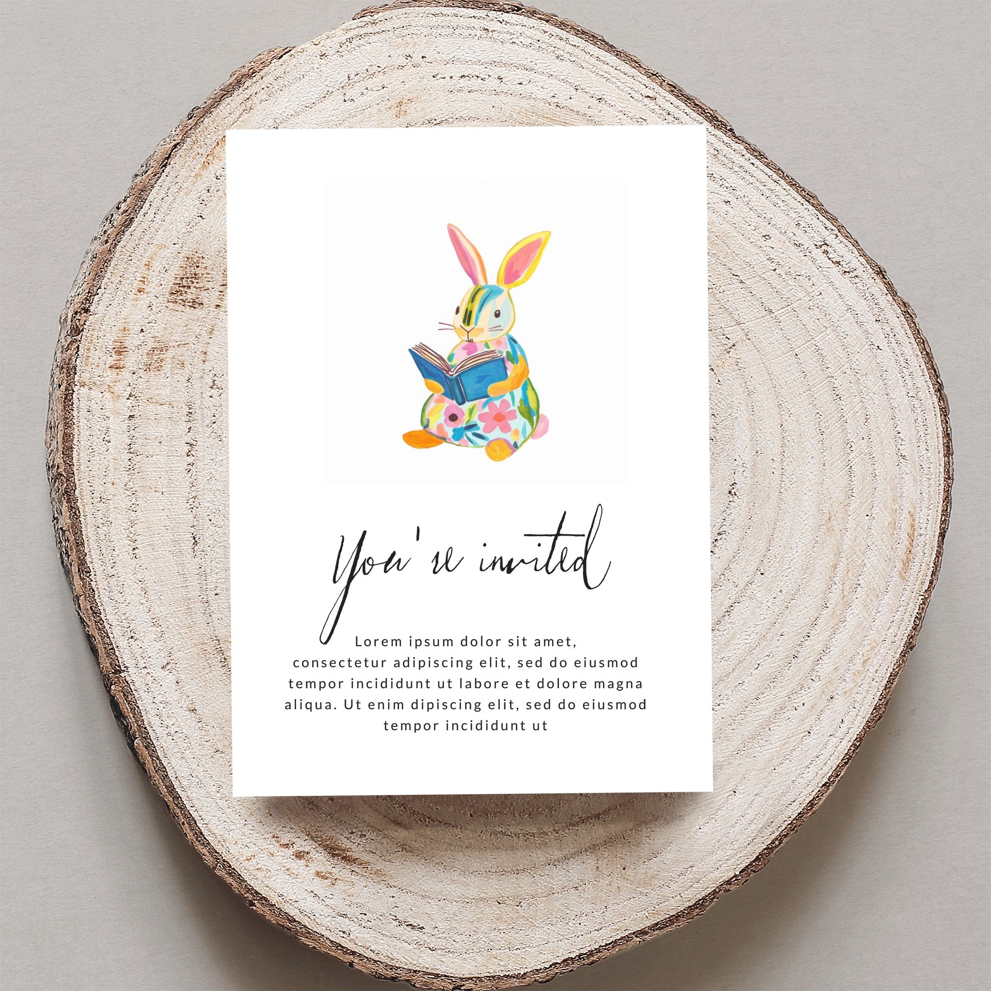 Invitation card with a colorful bunny reading a book, "You're invited" text.