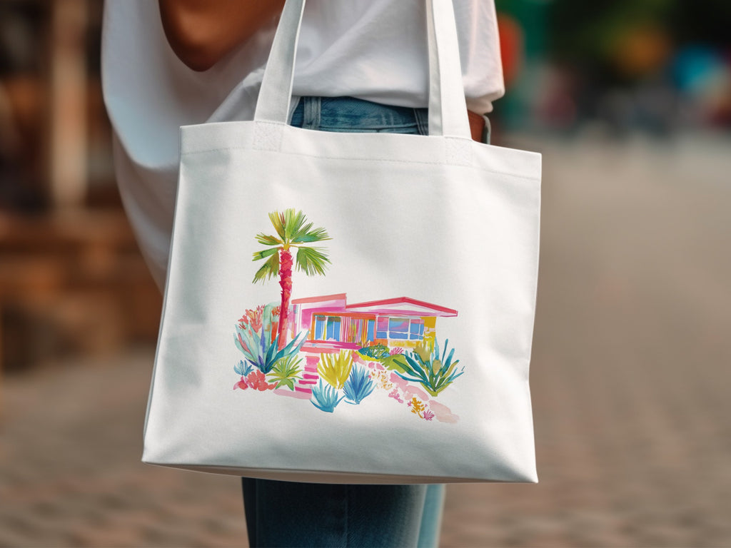 White tote bag with watercolor illustration of a pink mid-century modern house and desert plants.