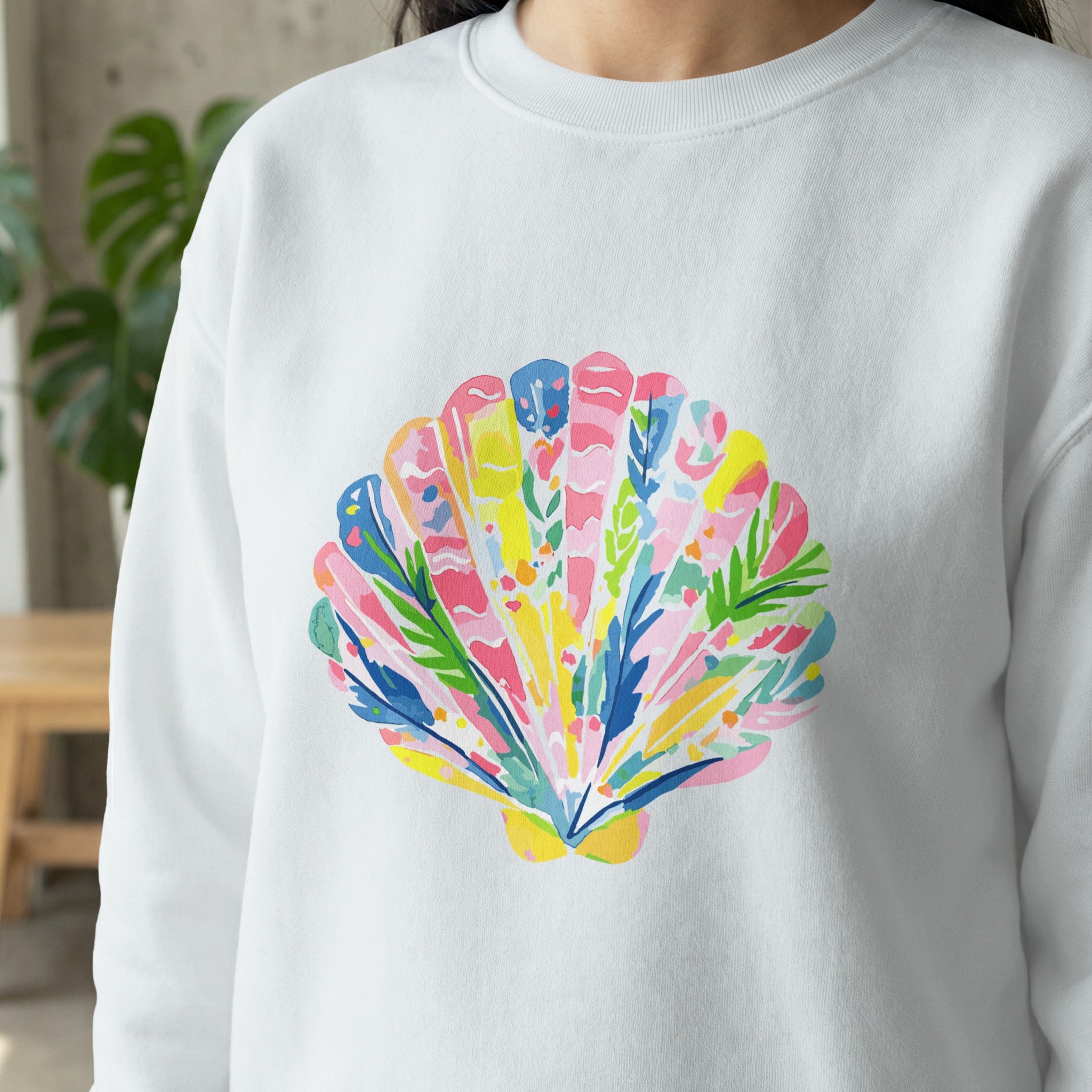White sweatshirt with colorful seashell illustration in pink, blue, and green.
