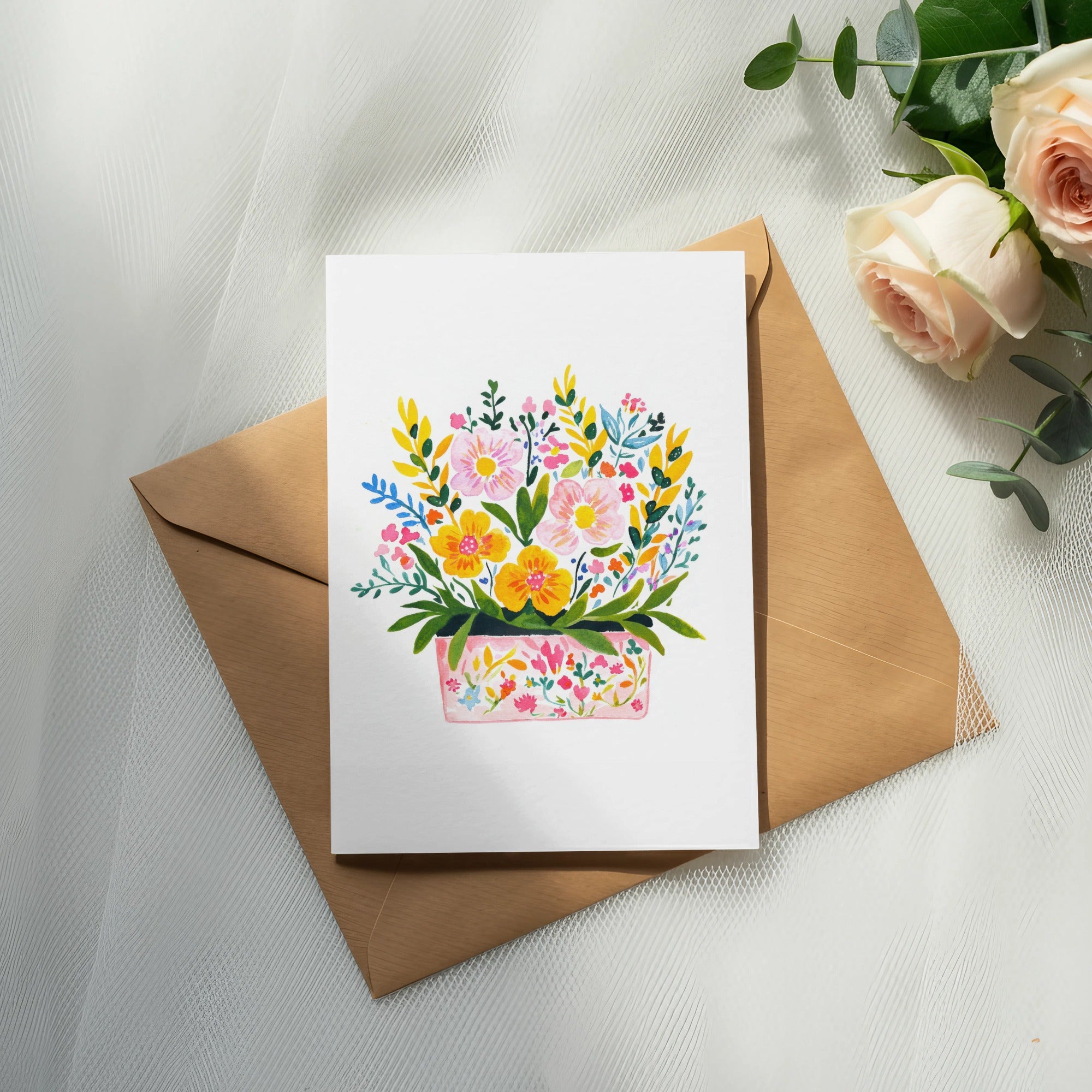 Watercolor floral arrangement on a white card atop a kraft envelope with roses.