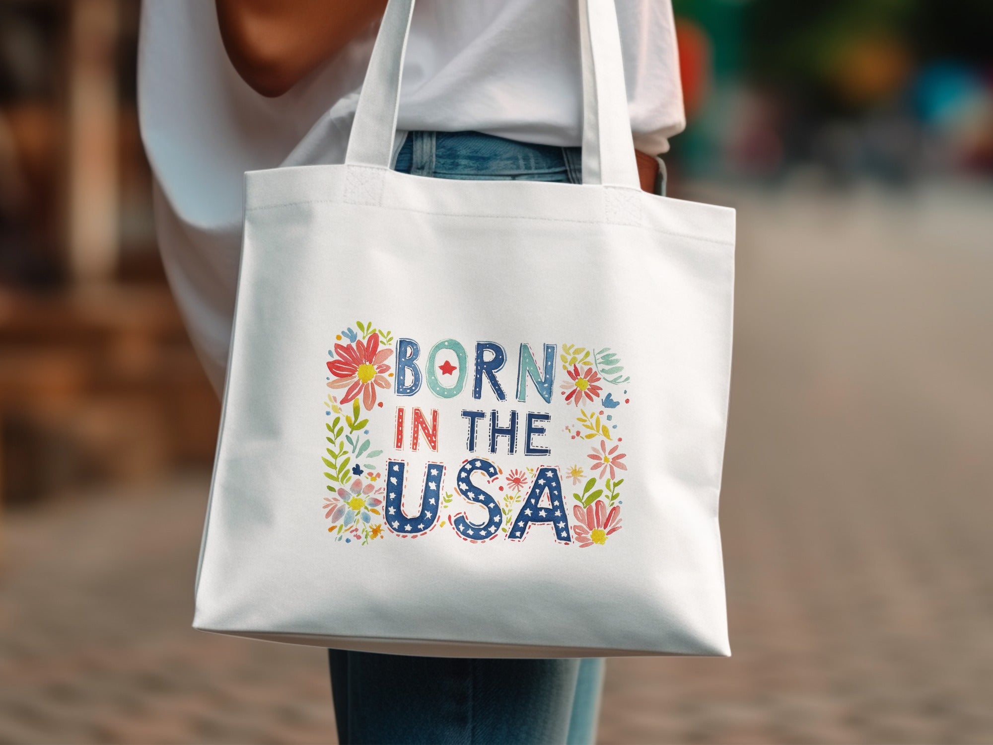 White tote bag with "Born in the USA" text and floral accents.