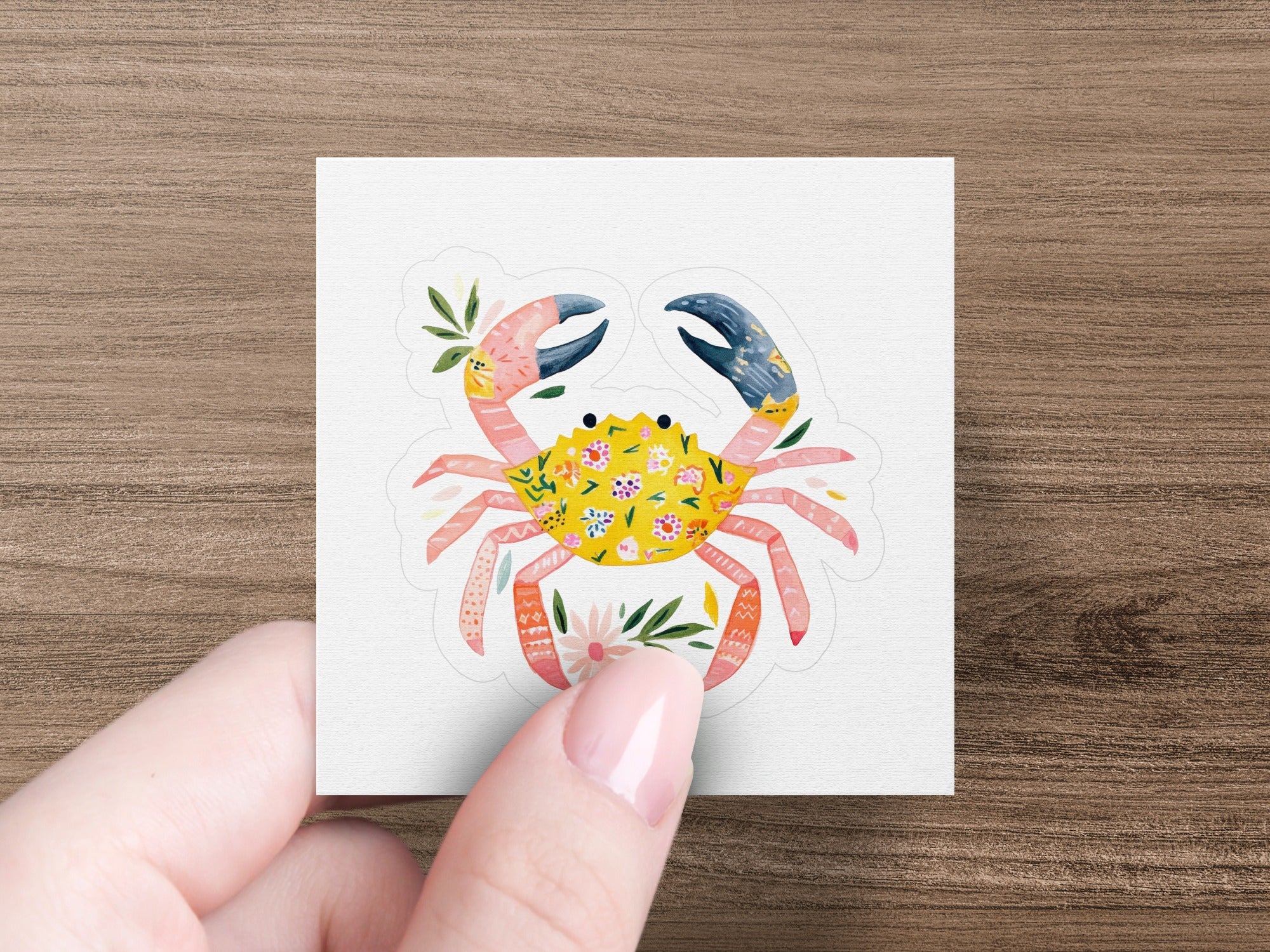 Crab sticker with floral pattern and foliage, held by a hand.