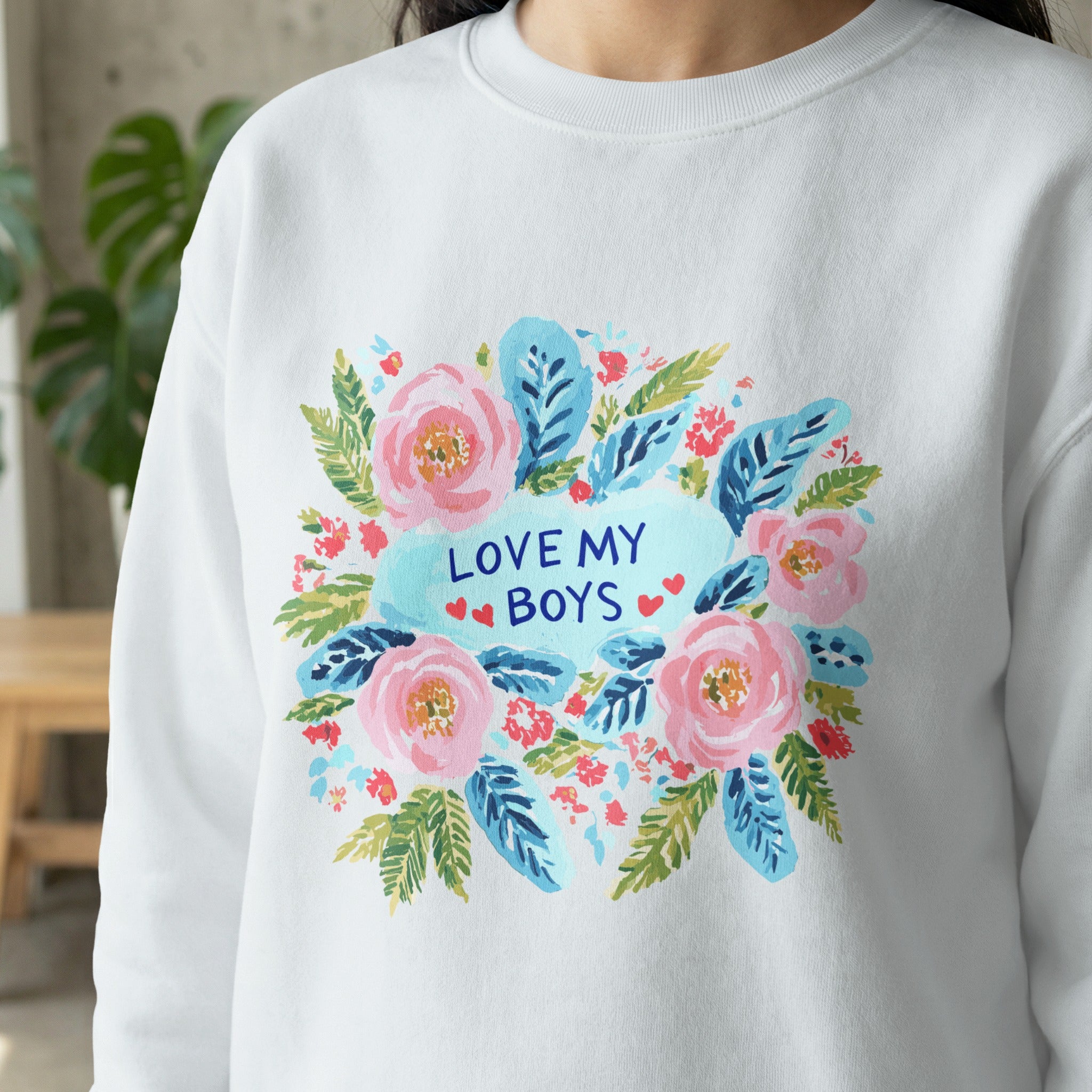 White sweatshirt with a floral wreath design and "LOVE MY BOYS" text.