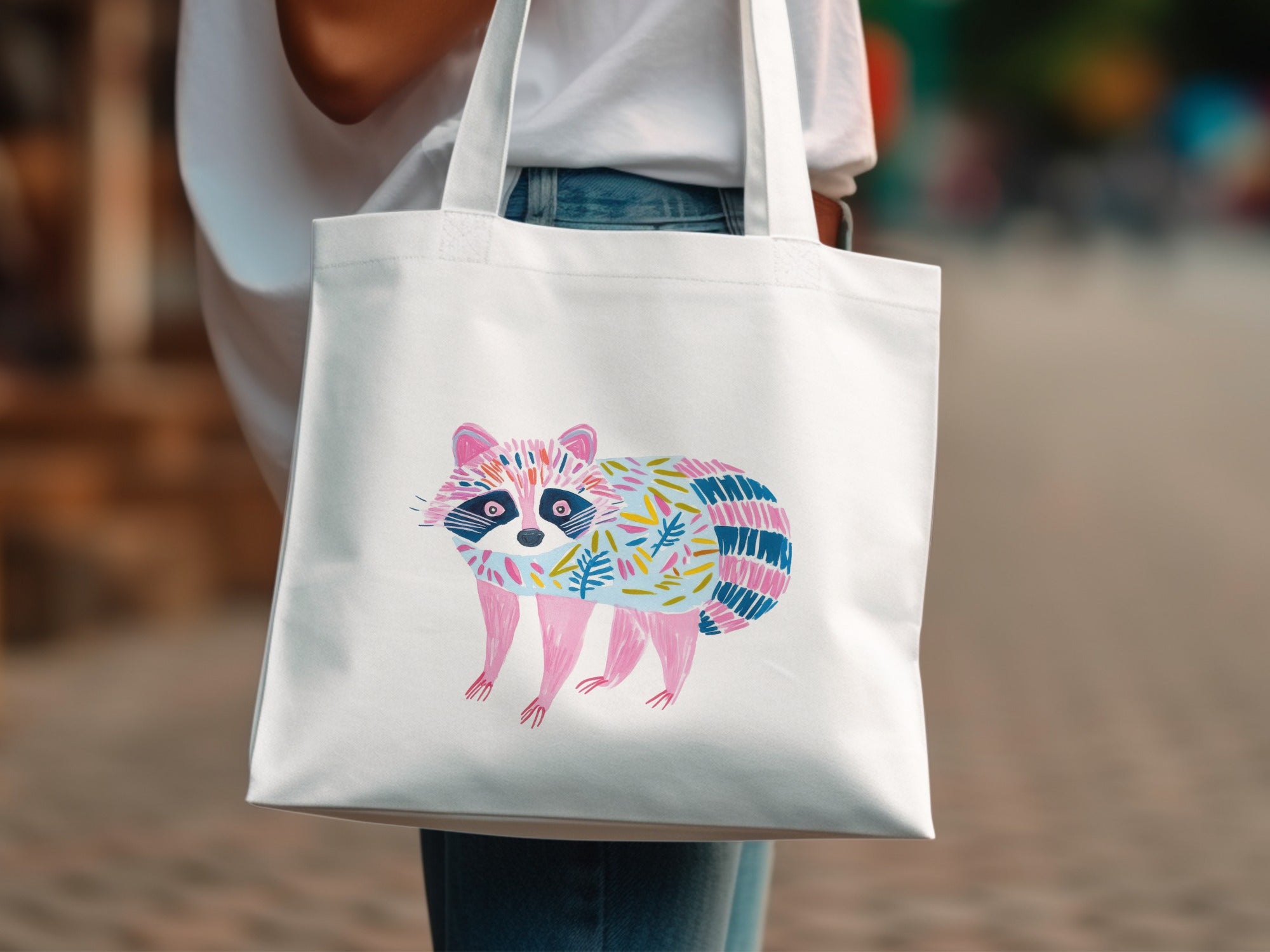 White canvas tote bag featuring a colorful, stylized raccoon illustration.