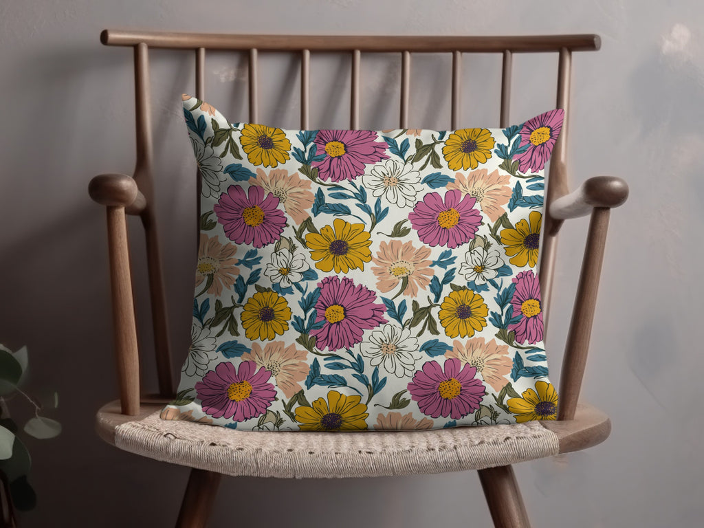 Floral throw pillow with pink, yellow, and white flowers on a wooden chair.