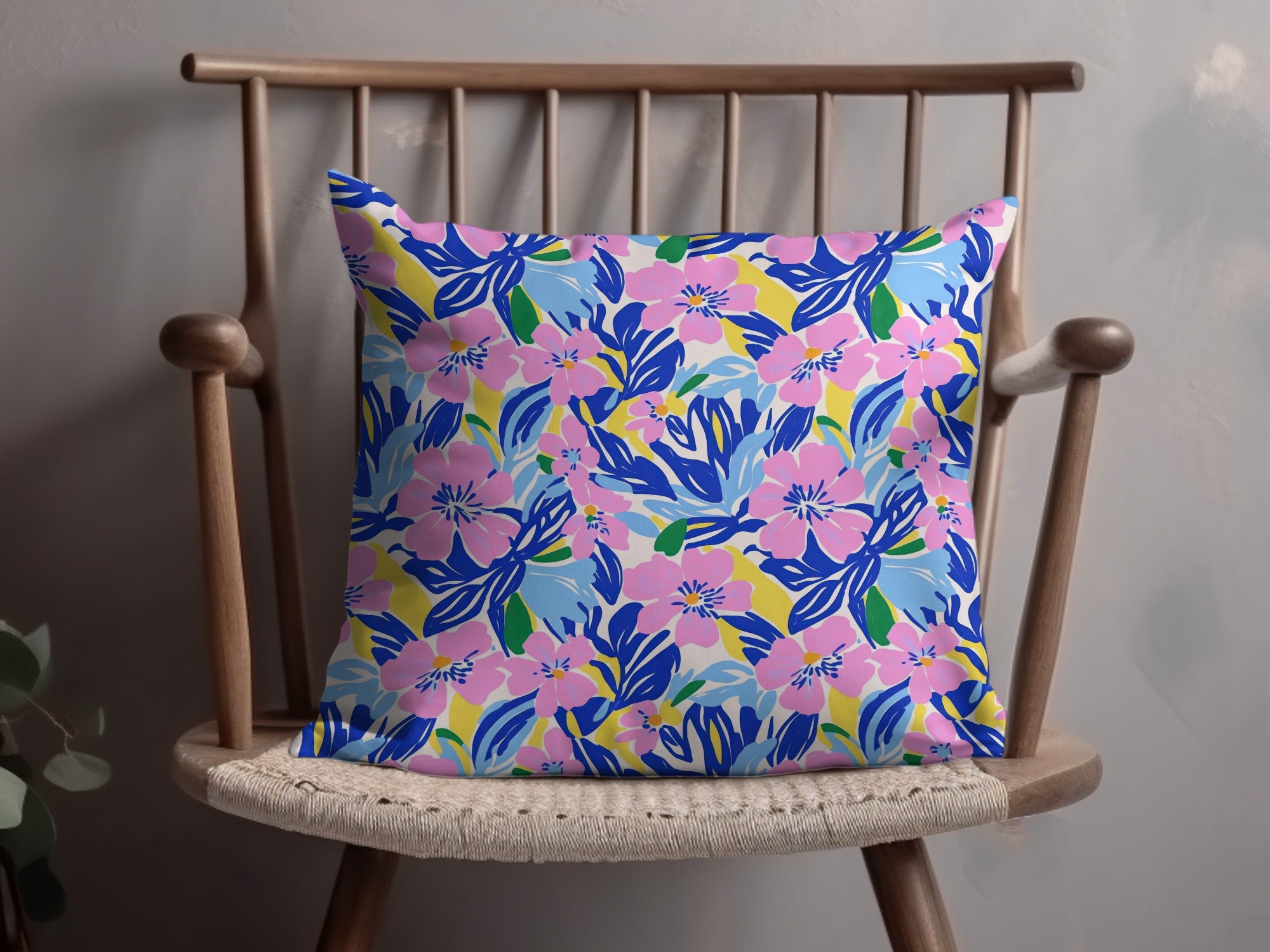 Pink and blue floral pattern on a throw pillow on a wooden chair.