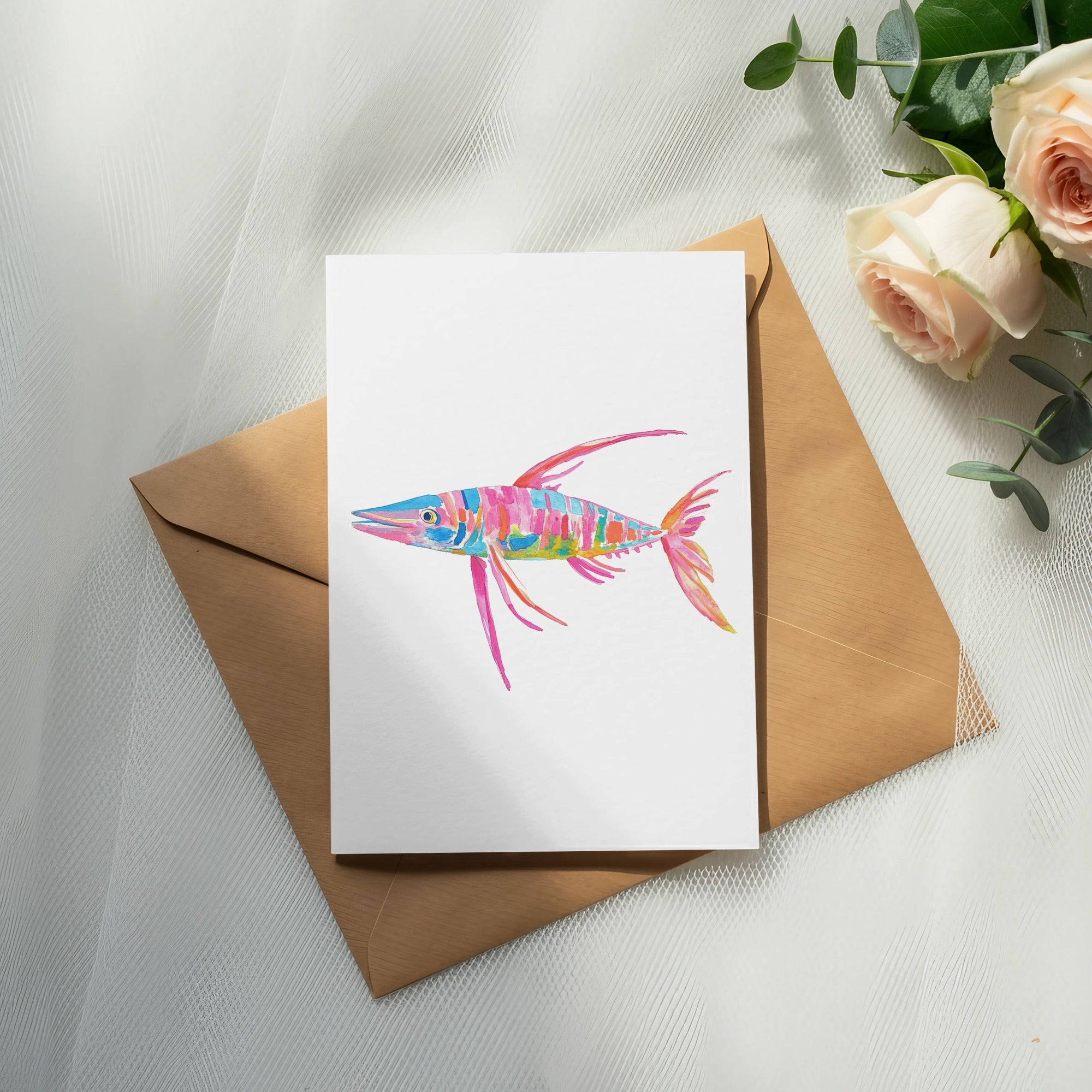 Colorful fish illustration on white card atop brown envelope with roses.