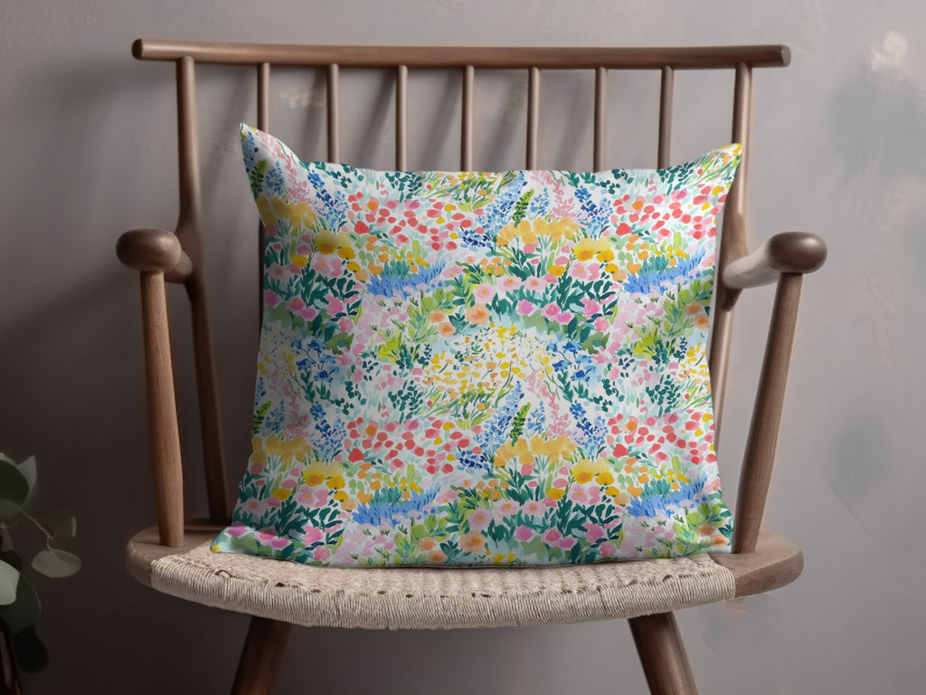 Floral pattern throw pillow with pink, blue, and yellow flowers on a wooden chair.