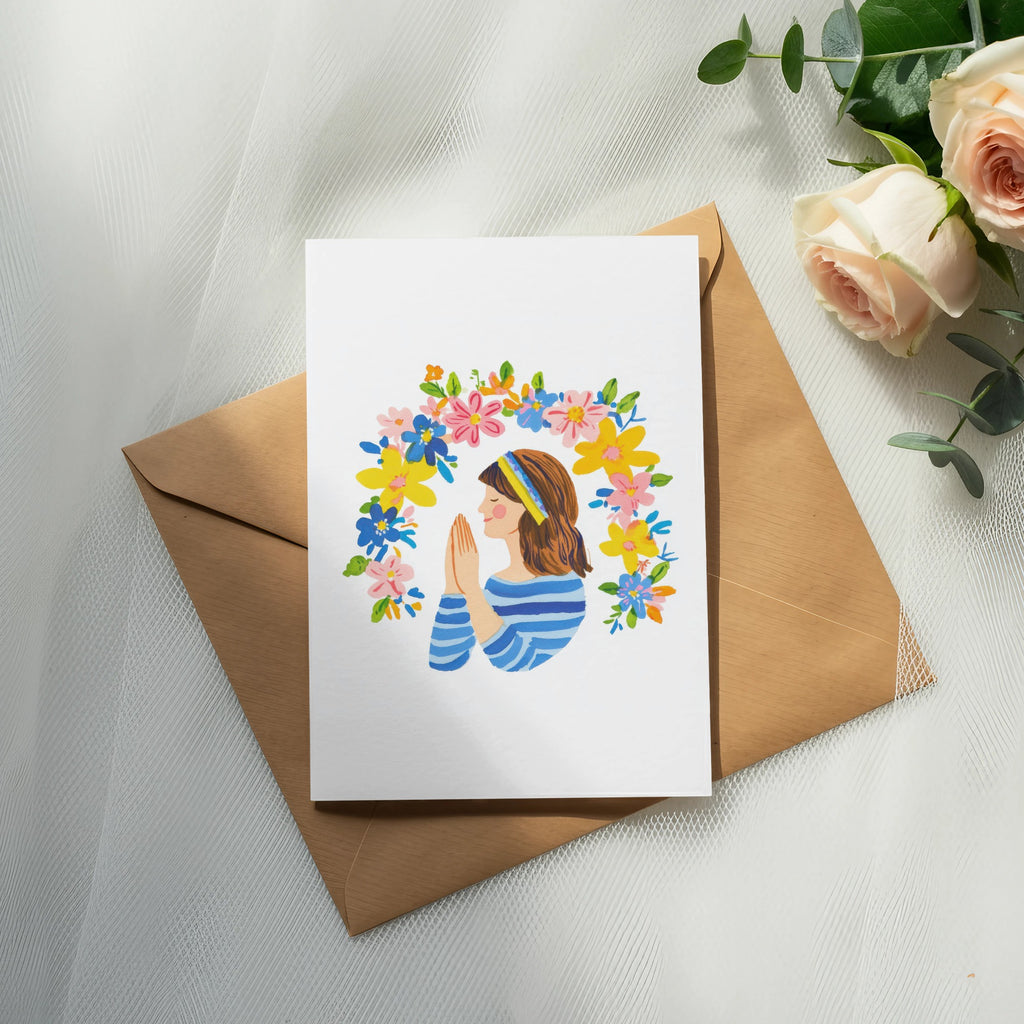 Card with woman in prayer surrounded by colorful flowers and Ukrainian flag colors.