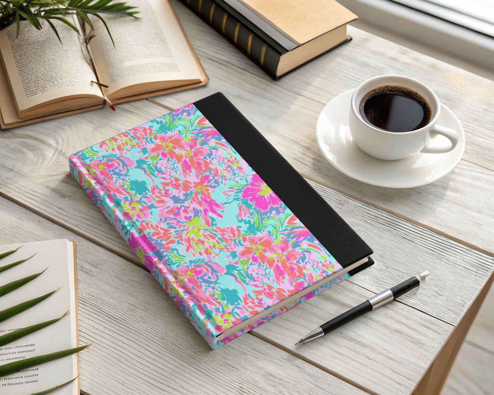 Colorful floral notebook with pen and coffee on a wooden desk.