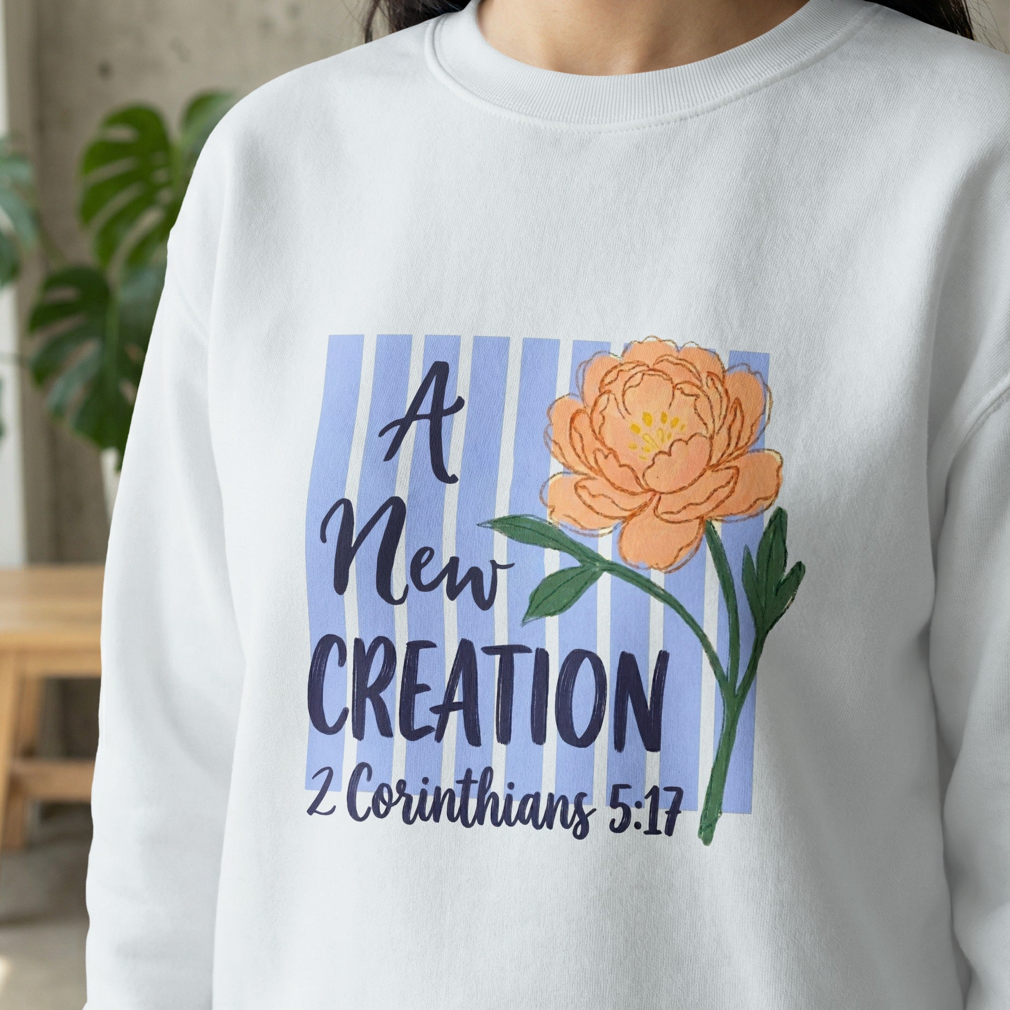 White sweatshirt with floral design and "A New Creation 2 Corinthians 5:17" text.