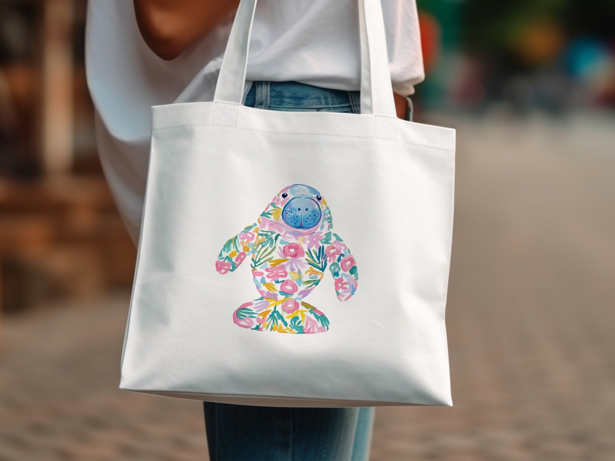 White tote bag with colorful floral manatee illustration.