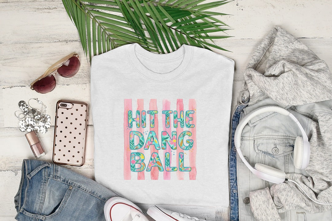 White t-shirt with "HIT THE DANG BALL" text on pink and white stripes.