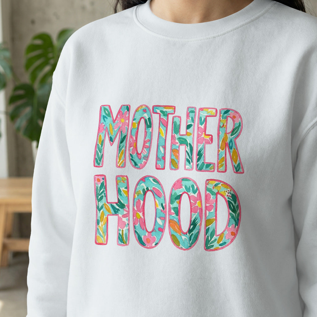 White sweatshirt with "MOTHERHOOD" in colorful floral letters.