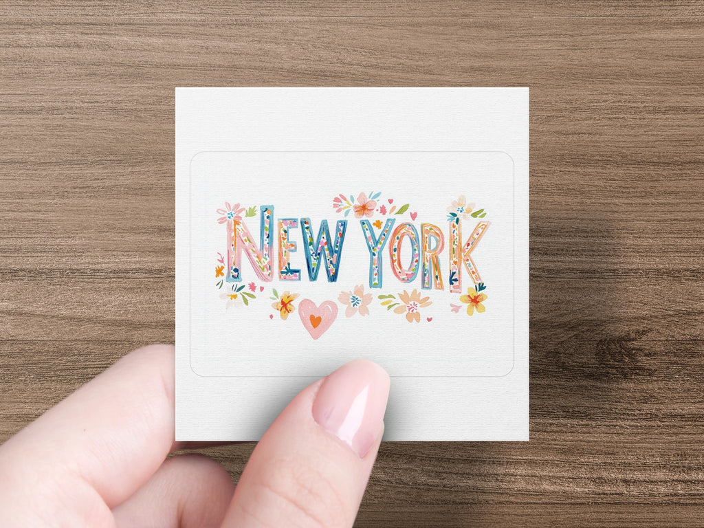 "NEW YORK" text with floral illustrations on a white sticker held by a hand.
