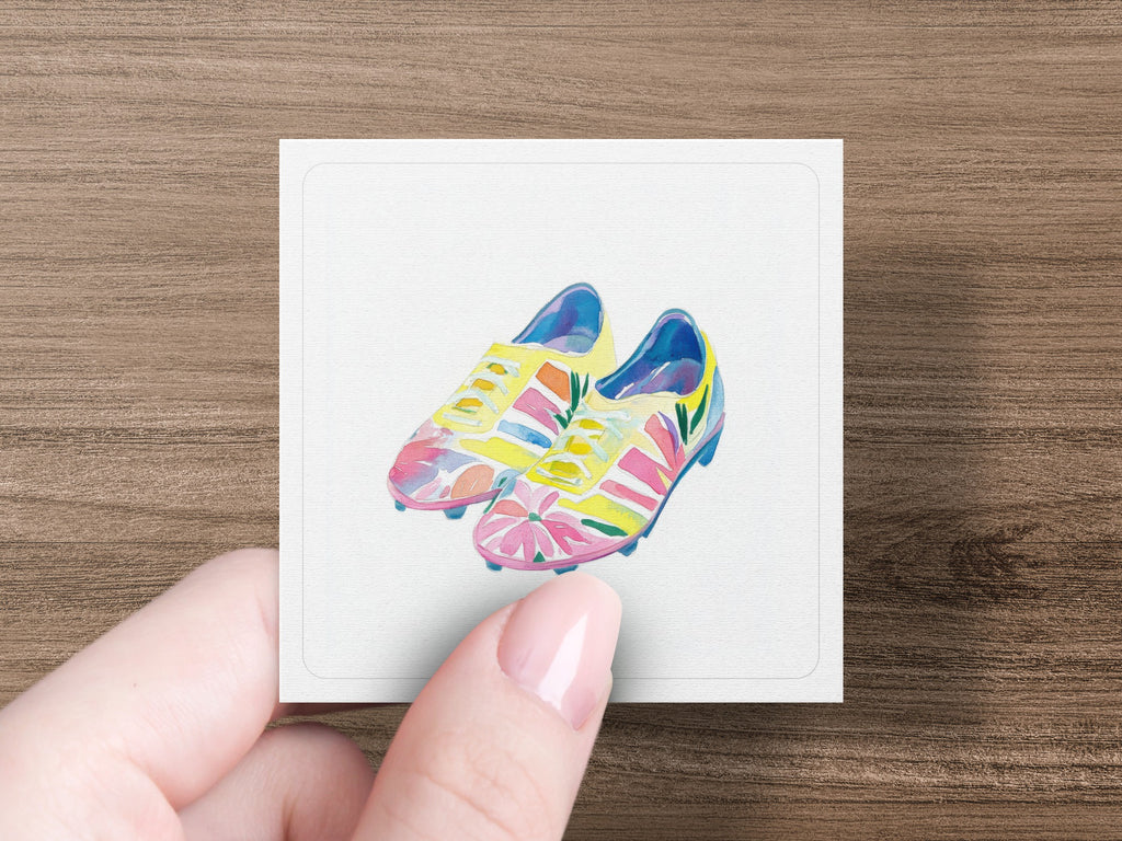 Colorful soccer cleats with floral accents on a white card.