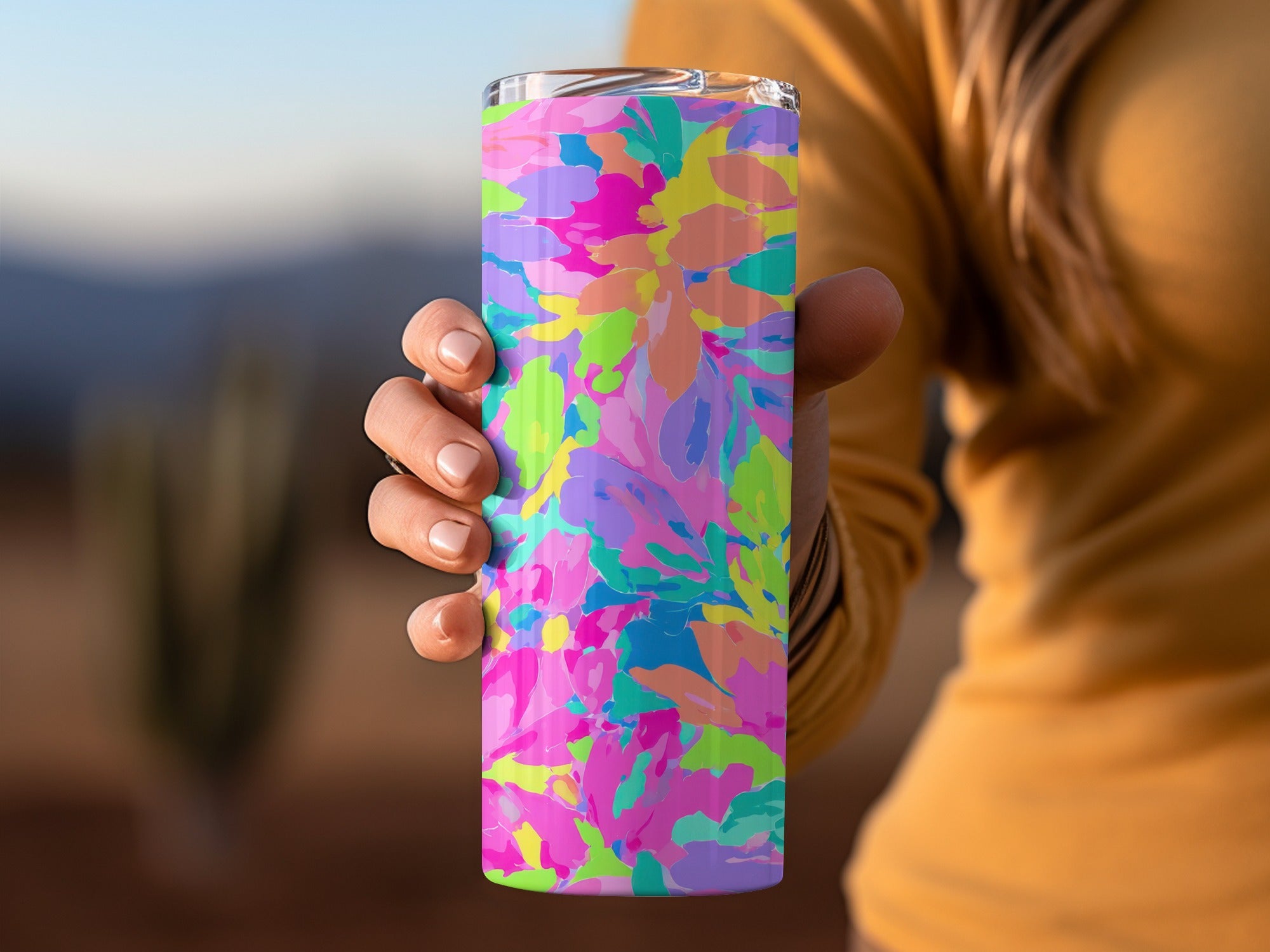 Hand holds colorful floral patterned tumbler with blurred background.