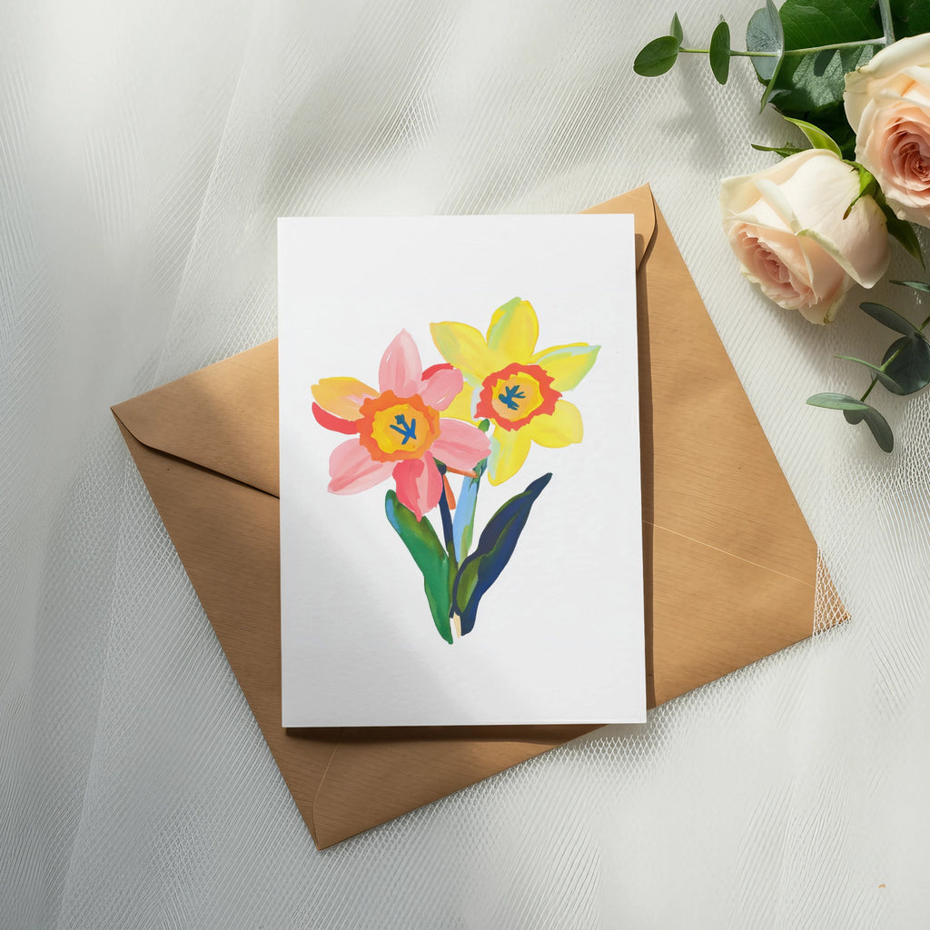Watercolor painting of pink and yellow daffodils on a card, with an envelope and roses.